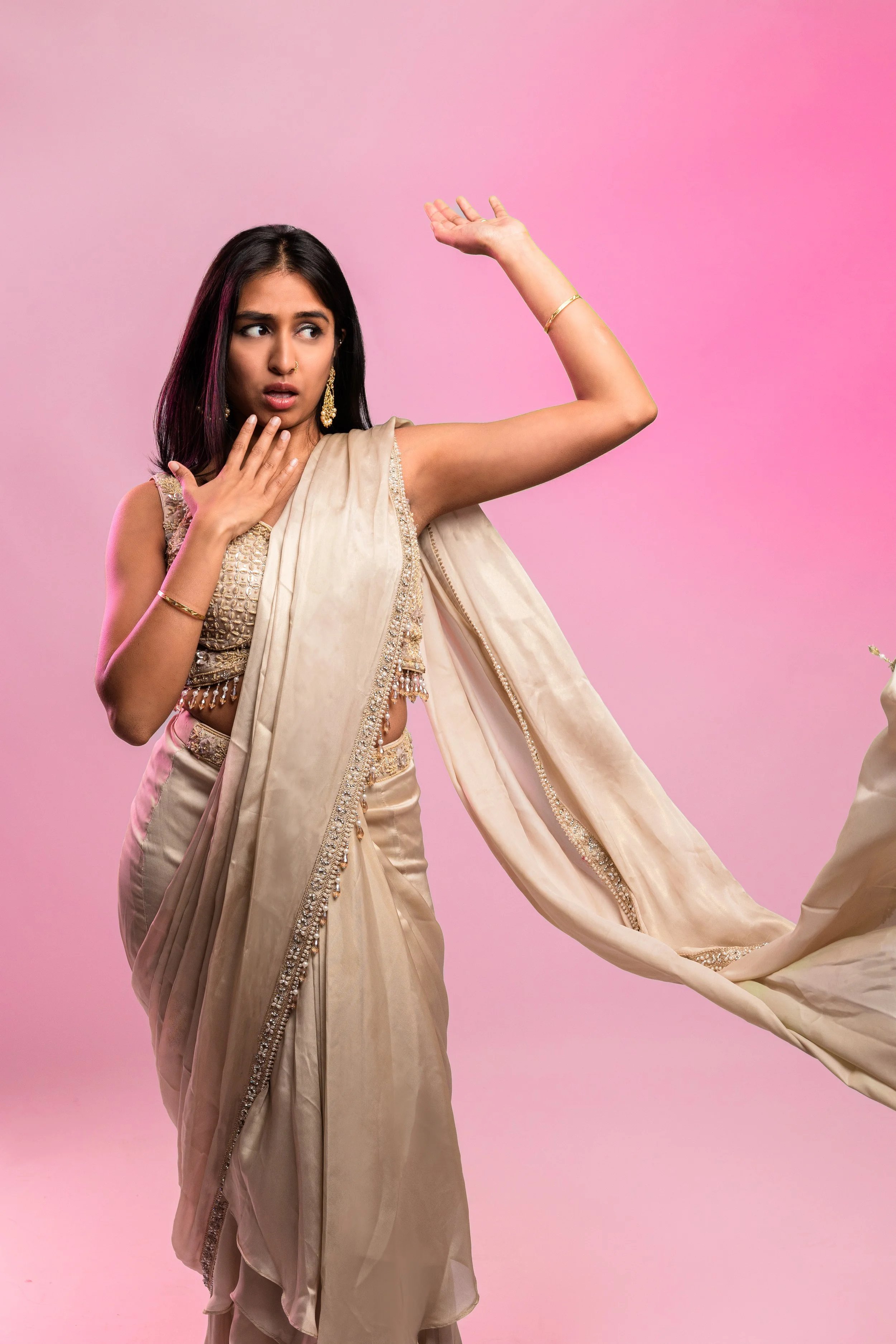 A woman in traditional beige Indian attire has a surprised or worried expression, touching her neck with one hand and raising her other arm.