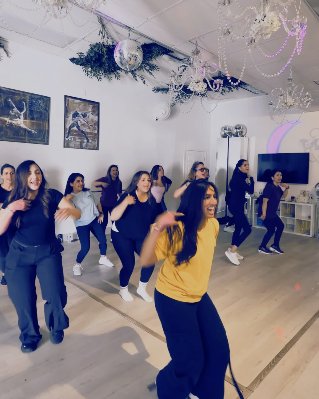 A group of women dancing and having fun in a decorated indoor space with disco balls, chandeliers, and framed pictures on the wall.