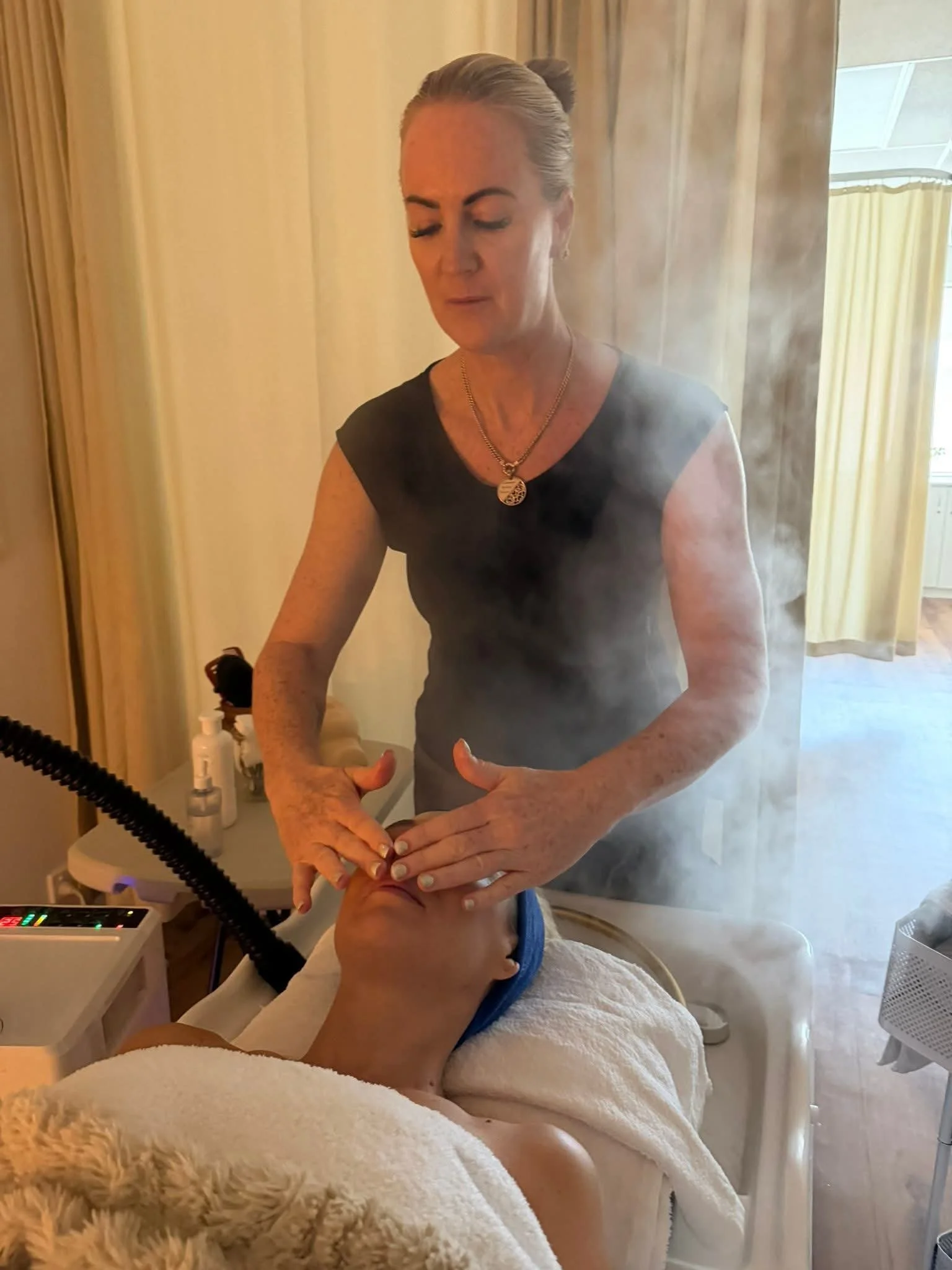 A woman receiving a facial treatment with steam, while lying on a therapy bed in a day spa.