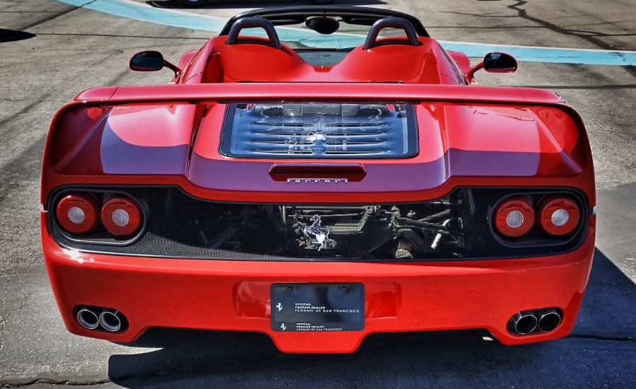 Red Ferrari sports car with rear view showing dual exhausts, circular taillights, and clear engine cover.