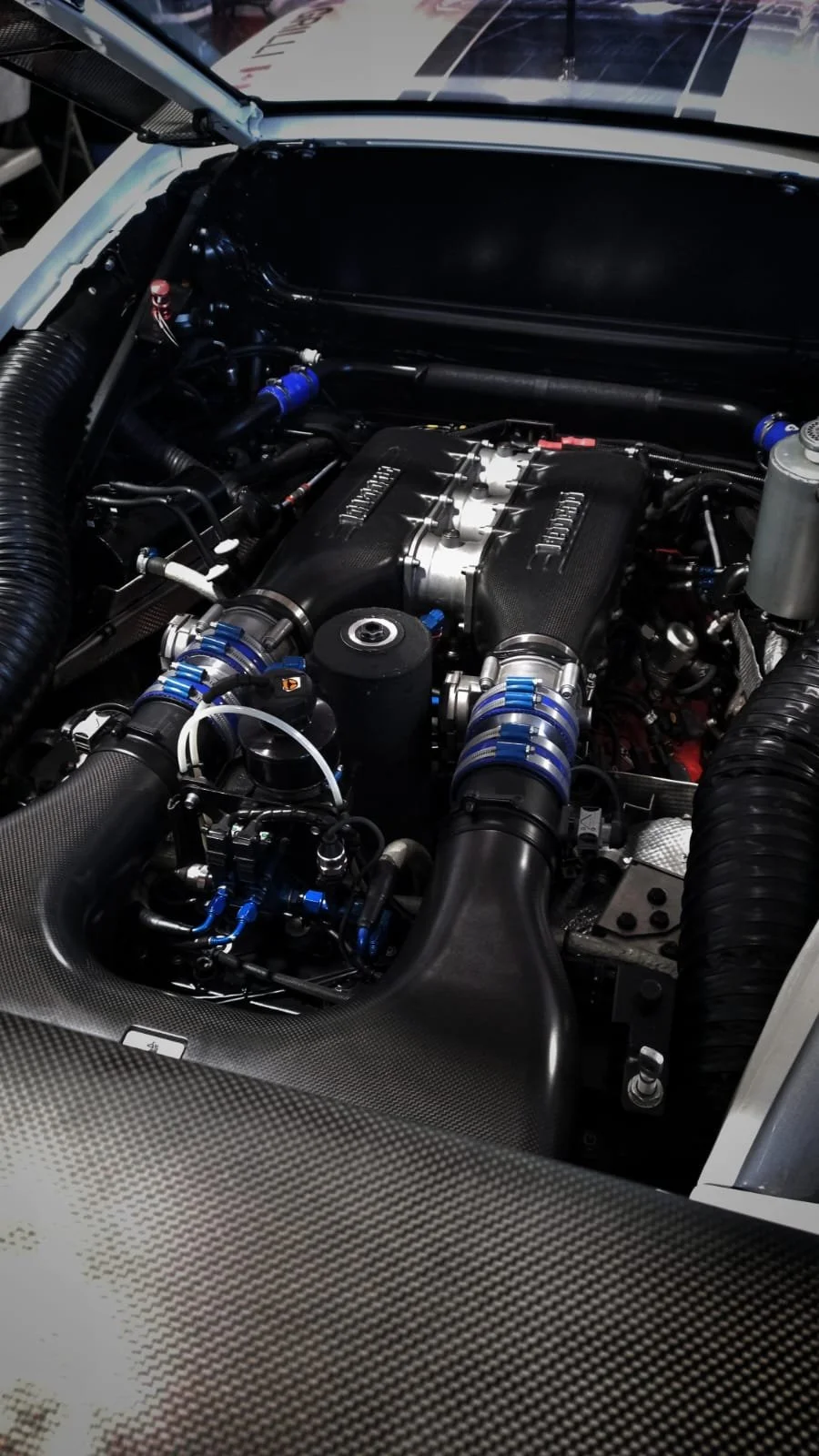 Close-up view of a high-performance race car engine with visible turbocharger components, pipes, and carbon fiber parts.