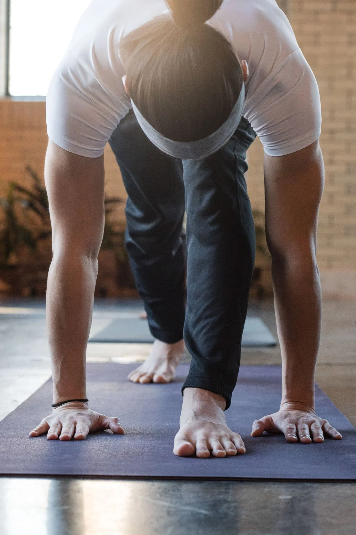 Person in a white shirt and black pants doing a yoga pose on a mat indoors.