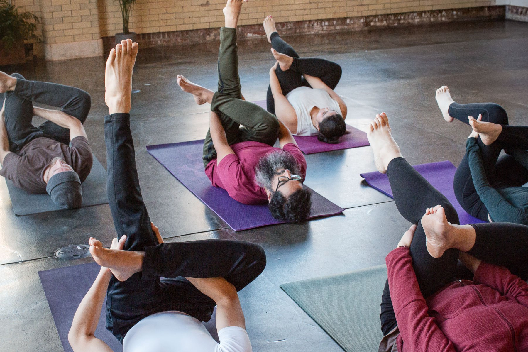 People practicing yoga indoors, lying on mats, and stretching, with some in a twist pose, in a relaxed group setting.