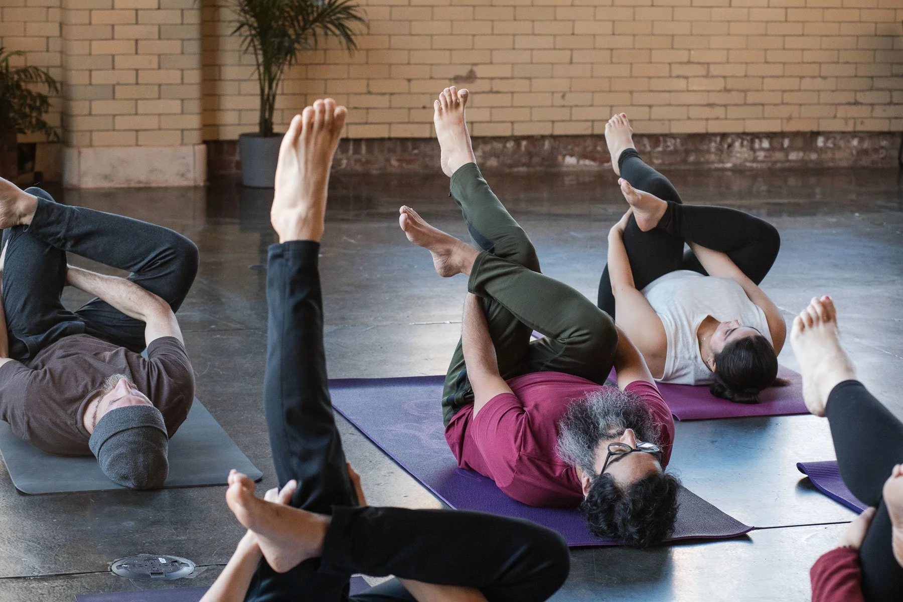People practicing yoga on mats in a studio with brick walls and plants.