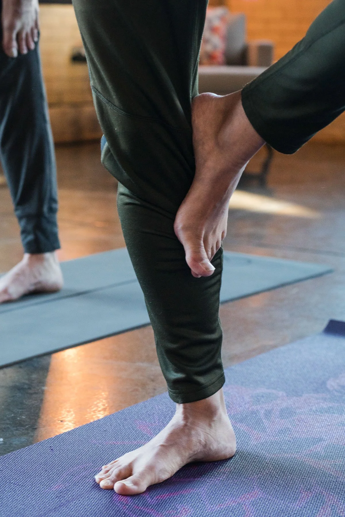 Person practicing yoga outdoors, balancing on one leg with hand on ankle, on yoga mat.