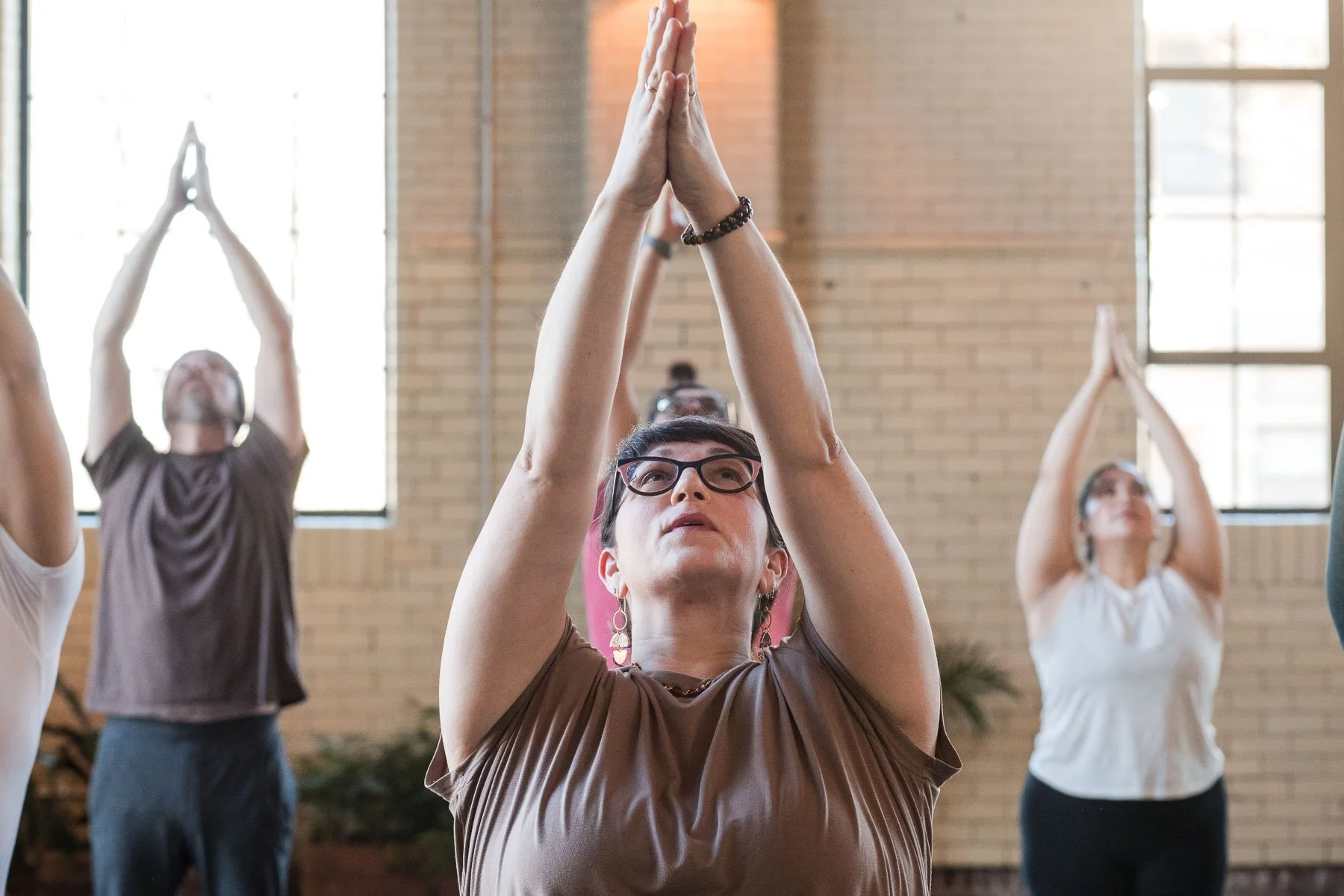 Group of people practicing yoga indoors with hands in prayer position overhead.