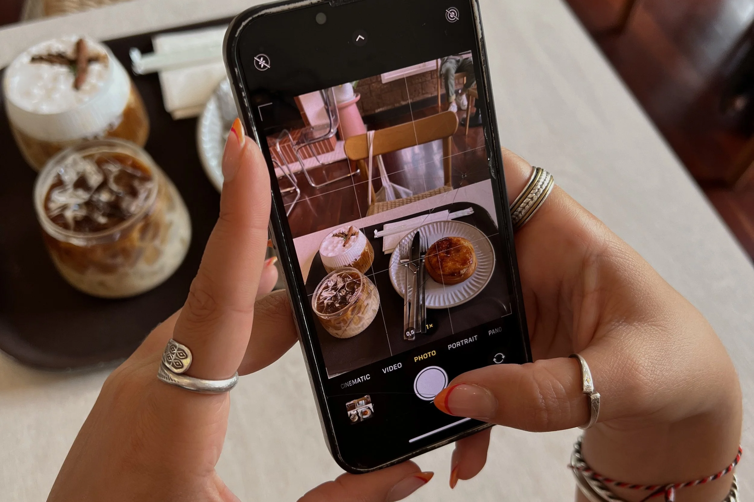 Person taking a photo of a table with two iced coffees, a cupcake, and a pastry in a cafe.