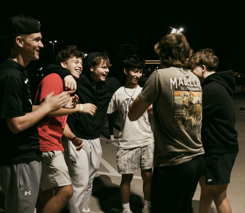 A group of six teenagers standing together at night, smiling and talking outdoors.