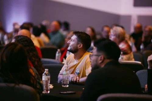 An audience seated at a conference or seminar, with people listening attentively to a speaker or presentation.