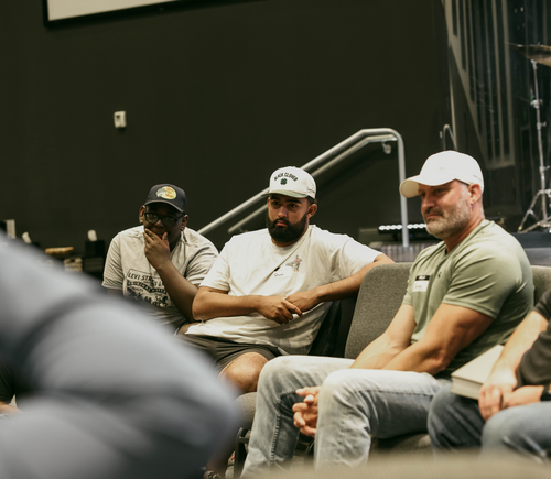 Three men sitting in a room, appearing to listen or participate in an event or discussion.