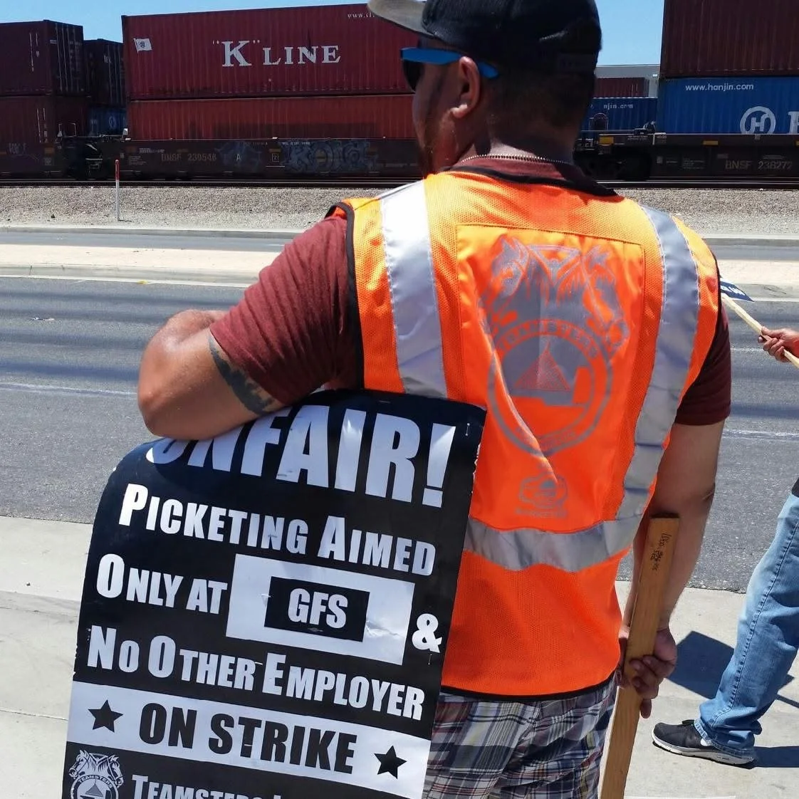 Chris Stout, union consultant & labor negotiator, on a strike line, wearing an orange safety Teamster vest, with a picket sign under his right arm. Sign says, "Unfair! Picketing Aimed Only at GFS & No Other Employer.  ON STRIKE." c. 2014.