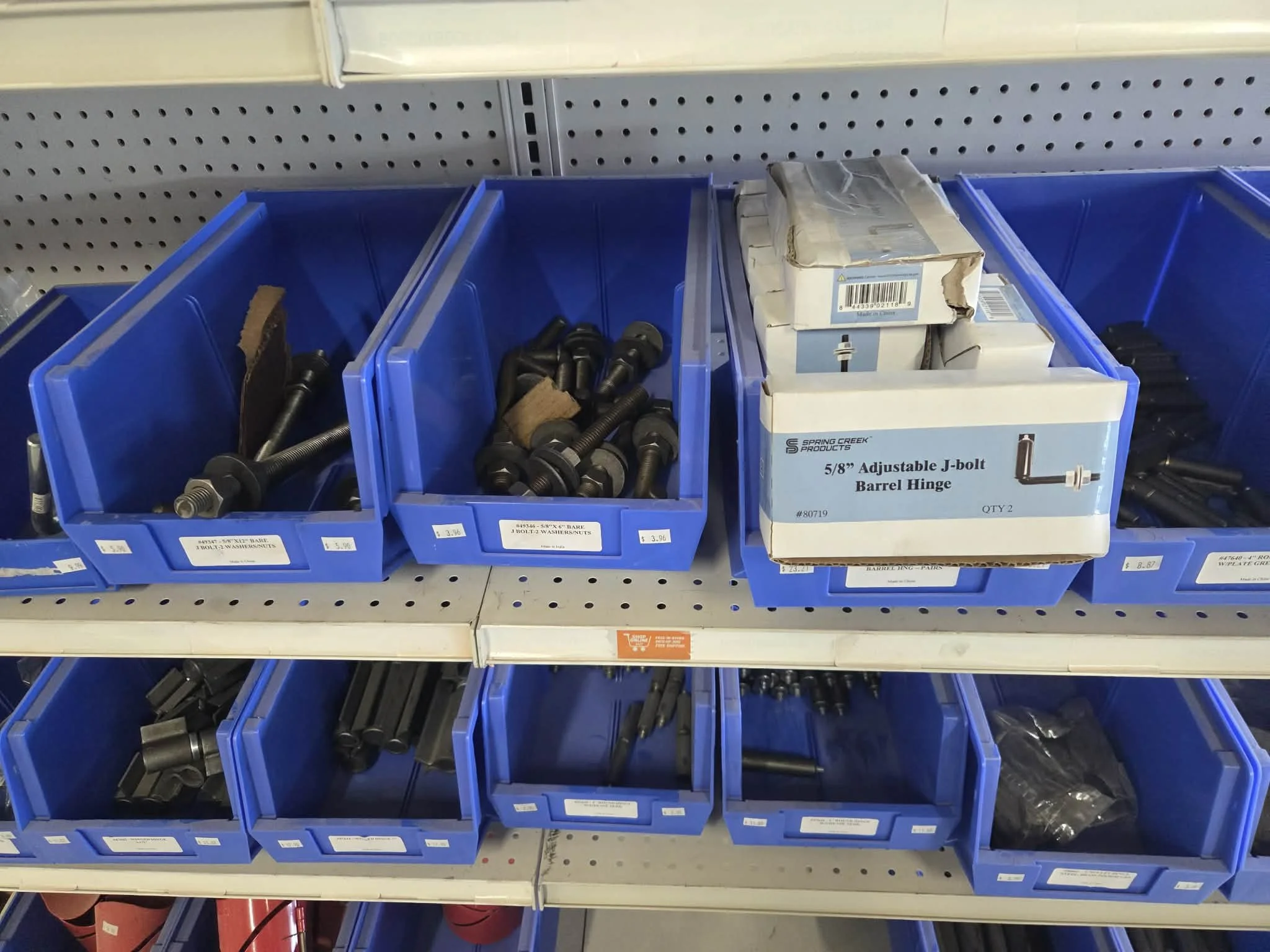 Blue plastic bins filled with assorted hardware pieces, including bolts, nuts, and brackets, on a store shelf.