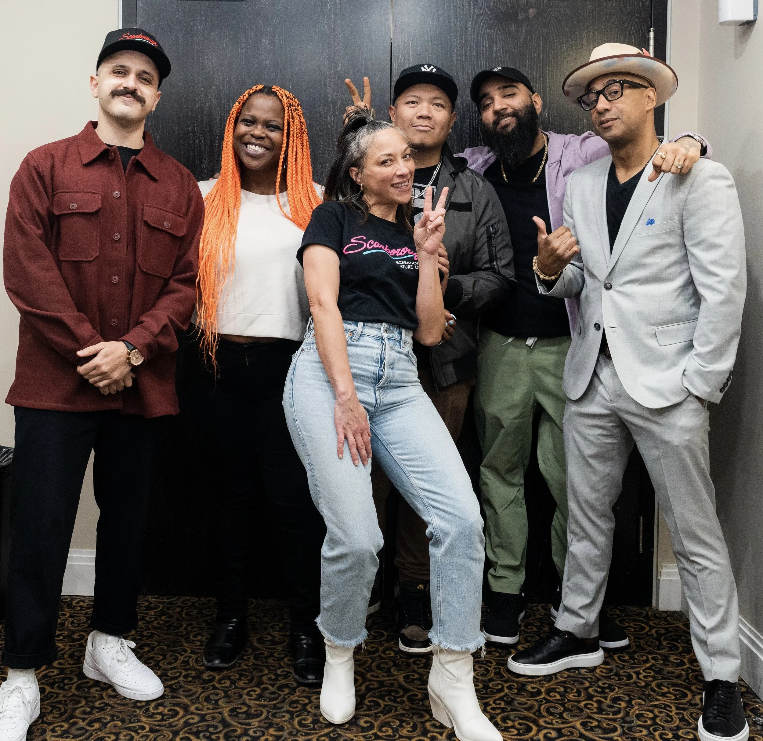 A diverse group of six people standing together indoors, smiling and posing for a photo.
