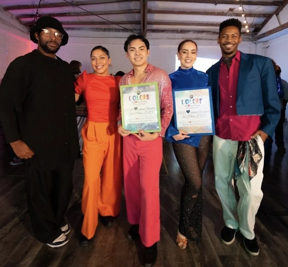 Group of five diverse people standing together indoors, holding framed certificates for a colorful event, and smiling at the camera.