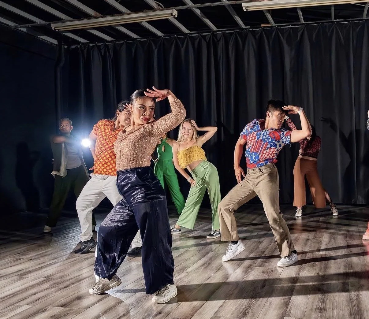 Diverse group of people dancing in a studio with black curtains and wooden floor.