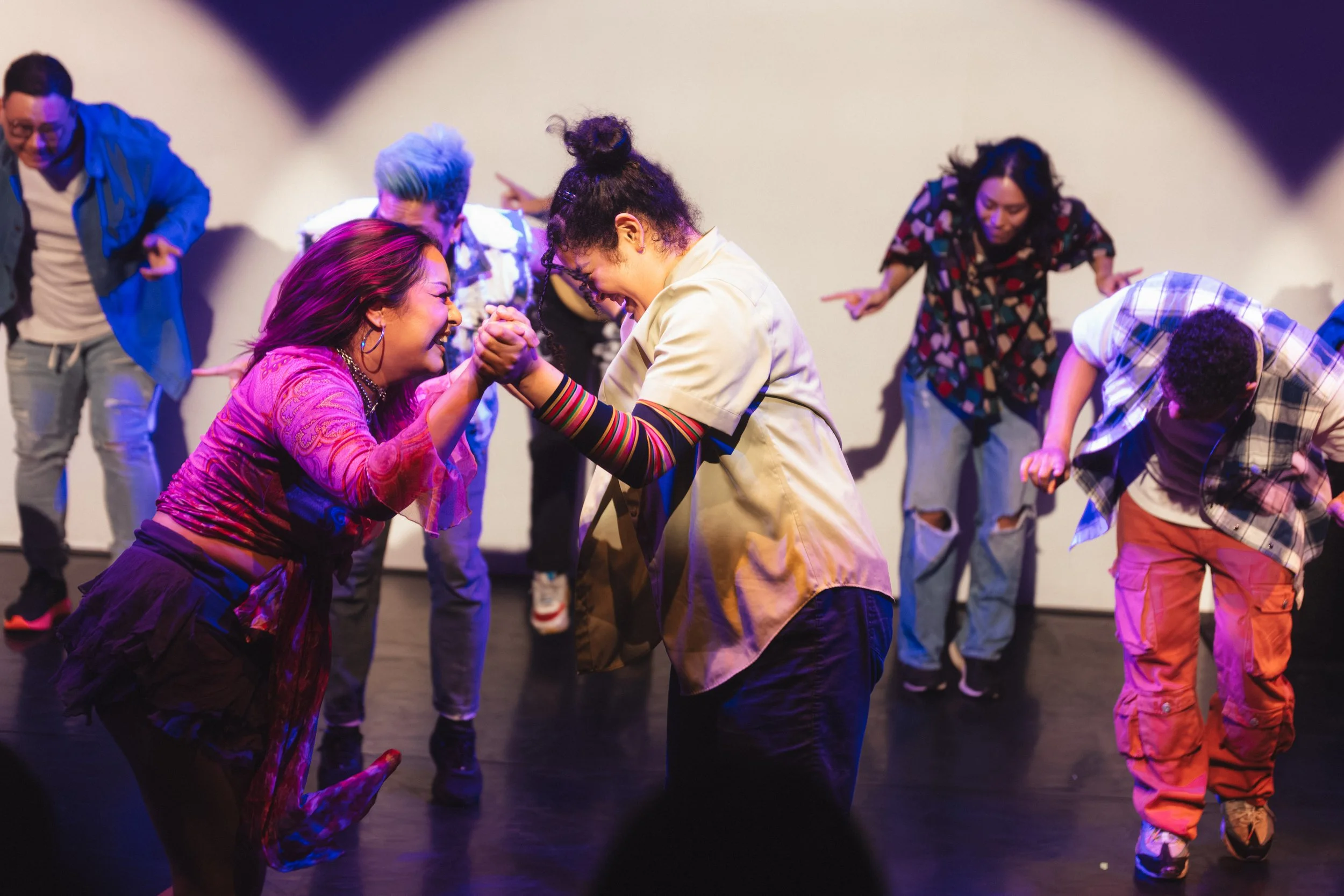 Group of diverse people dancing and enjoying themselves on stage with colorful lighting.