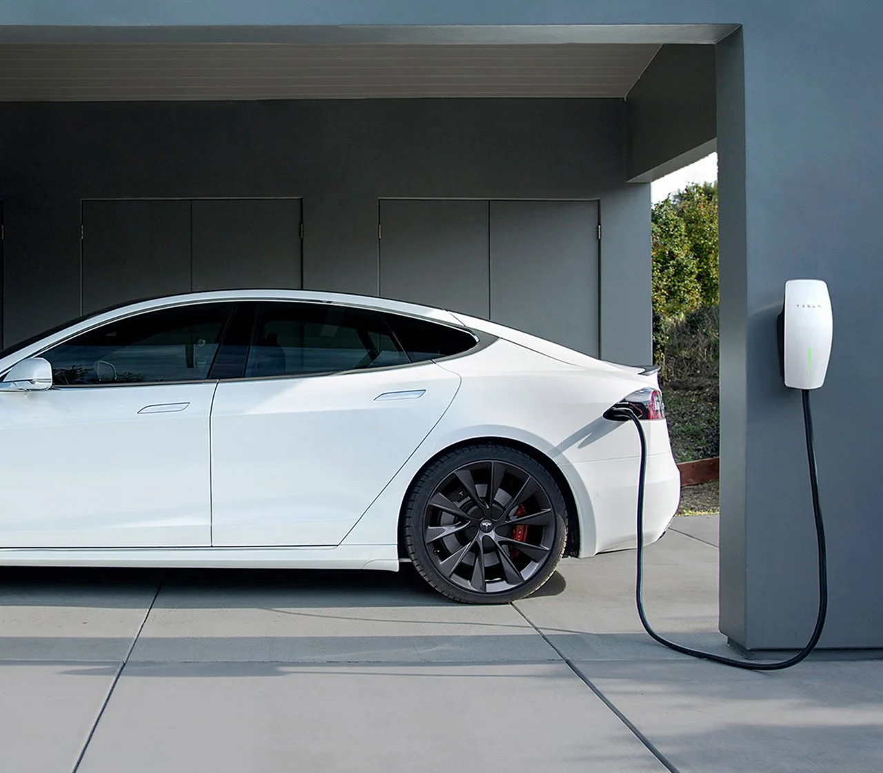 White Tesla Model S plugged into a home charging station in a residential garage.