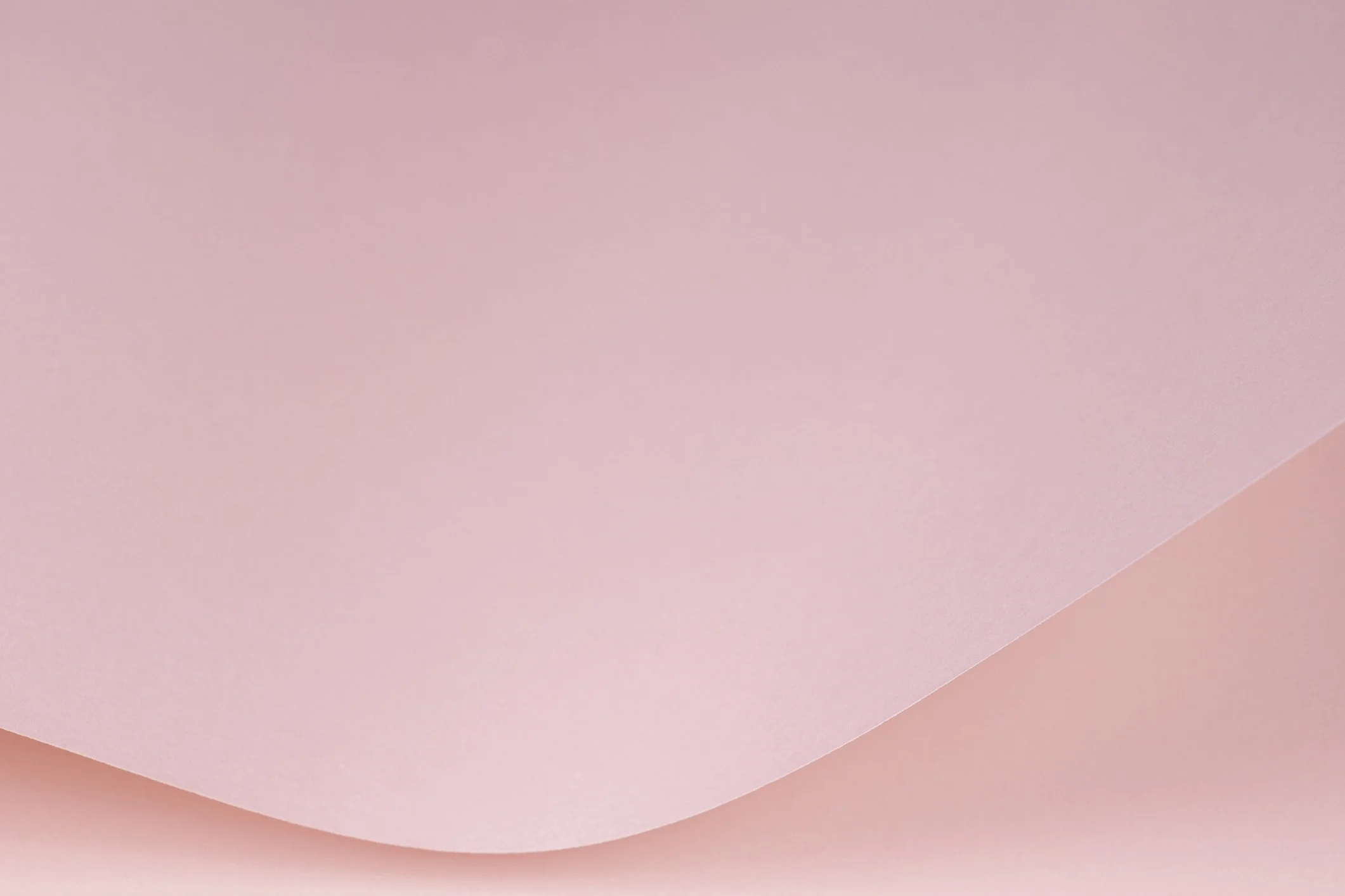 Close-up photograph of a soft pink gradient background with smooth curves and a subtle texture.