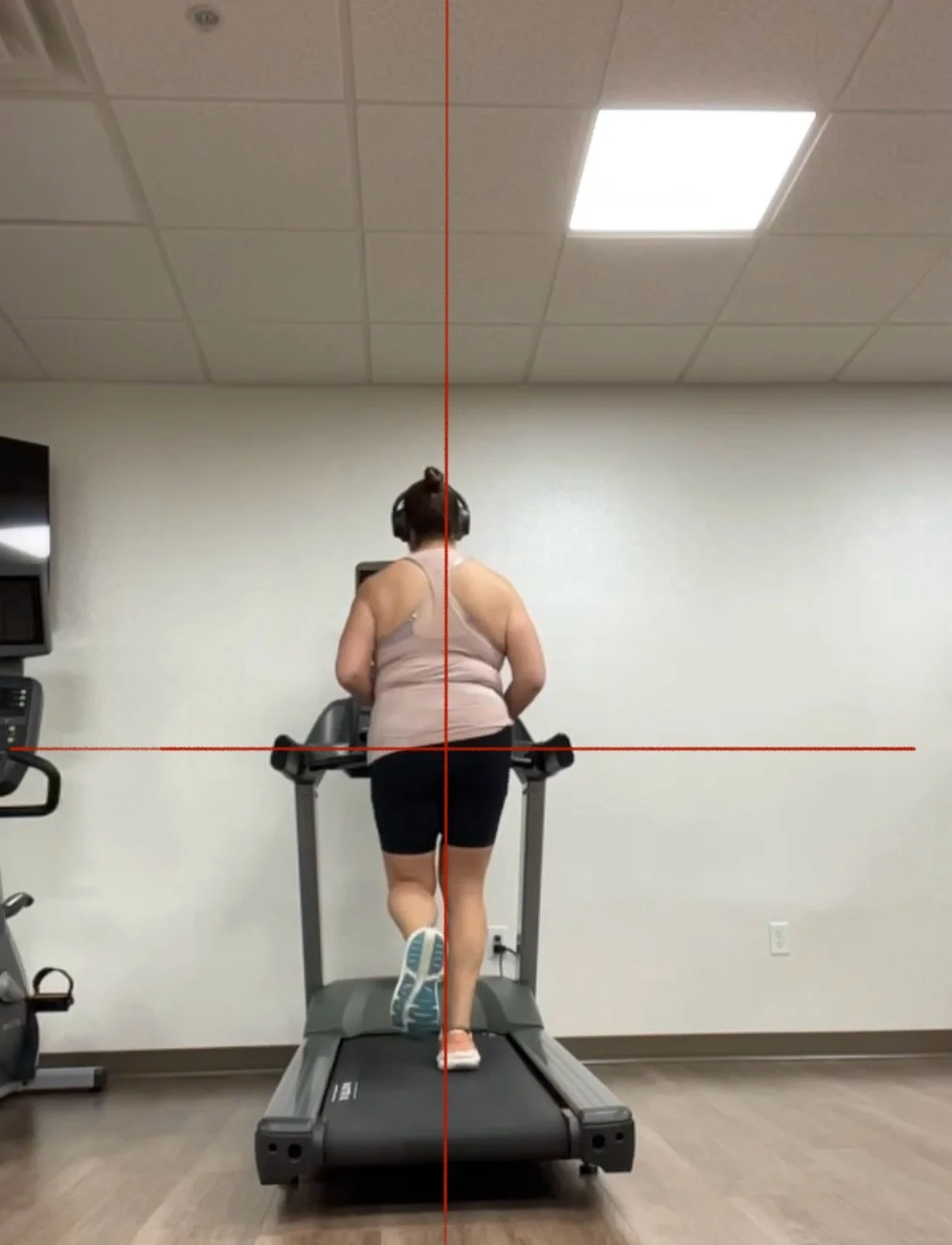 Woman running on a treadmill in a gym, wearing headphones and a tank top.