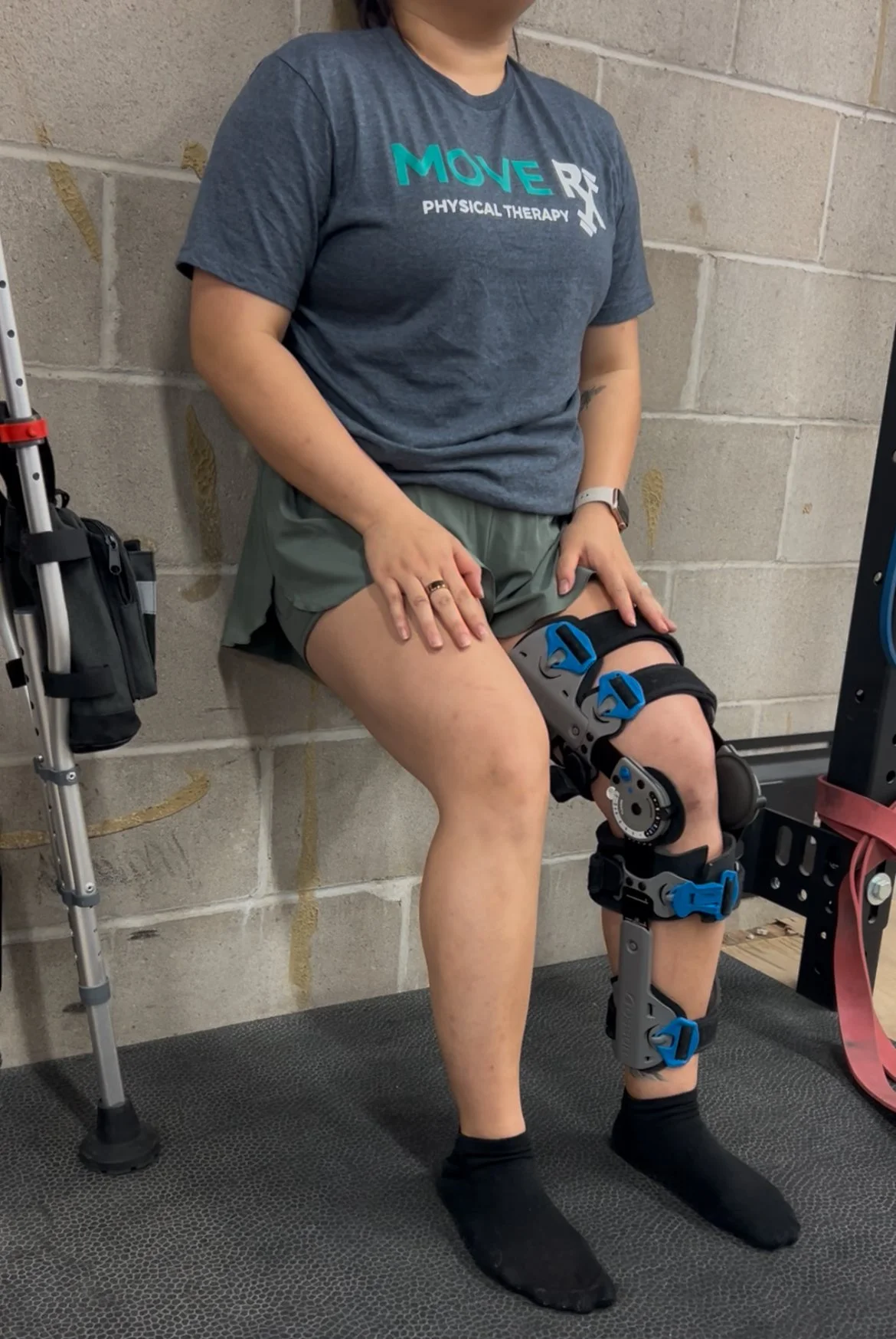 A person doing a wall sit with an ACL tear knee brace and a robotic knee exoskeleton on their right leg, in a therapy or rehabilitation setting.