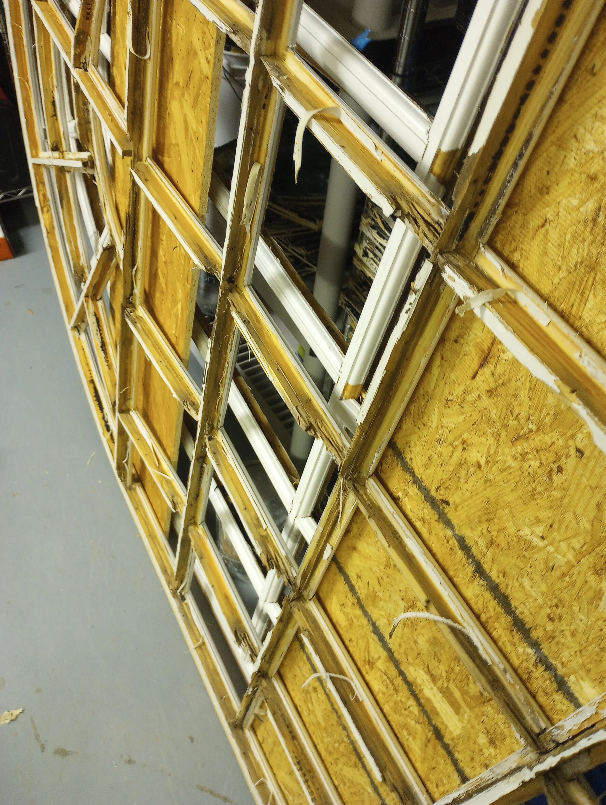 Dismantled window frames stacked on a blue-painted wooden surface in a workshop or storage area.