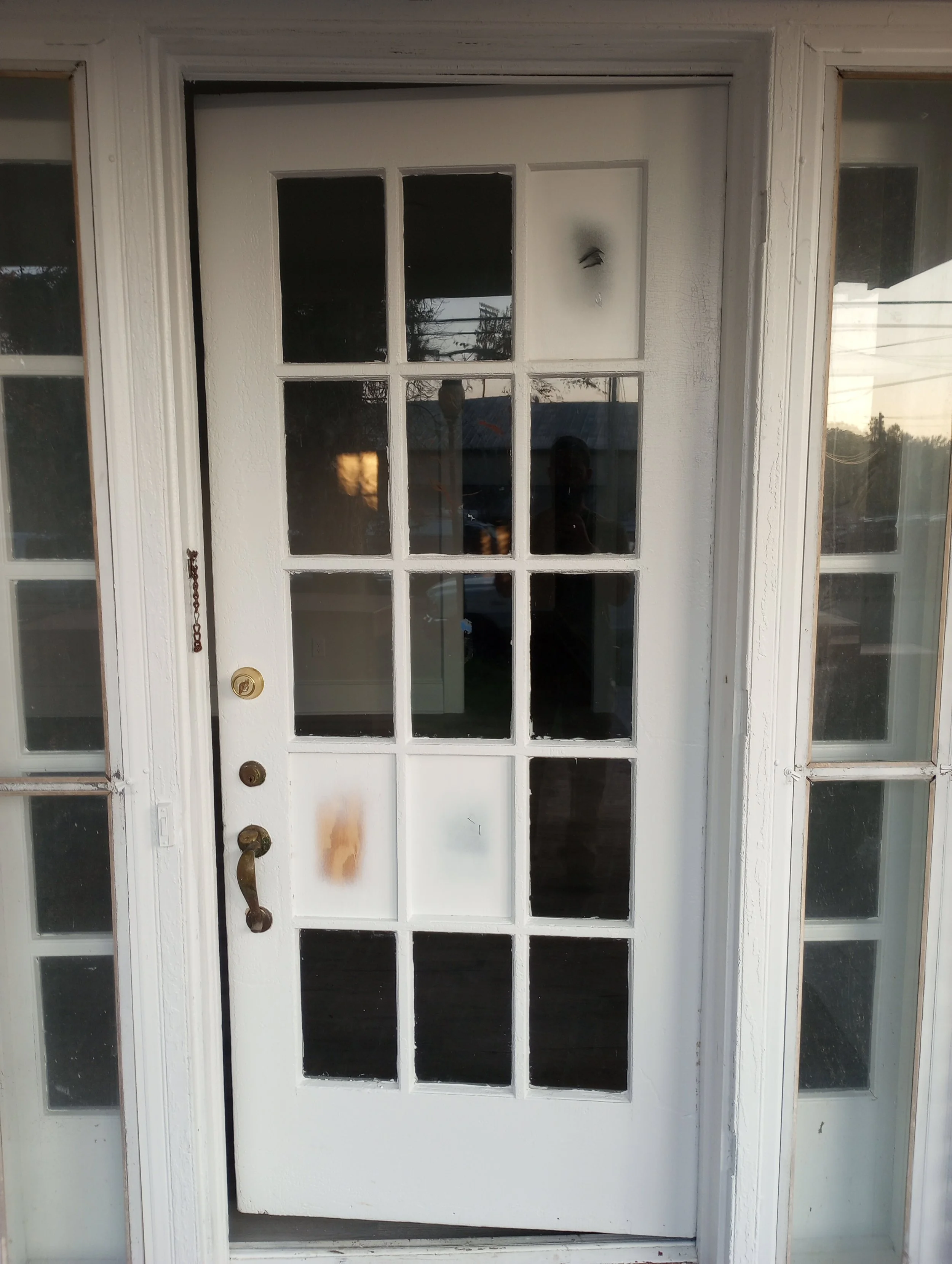 White door with glass panes, surrounded by sidelights, with a brass handle and a deadbolt, in a porch area.
