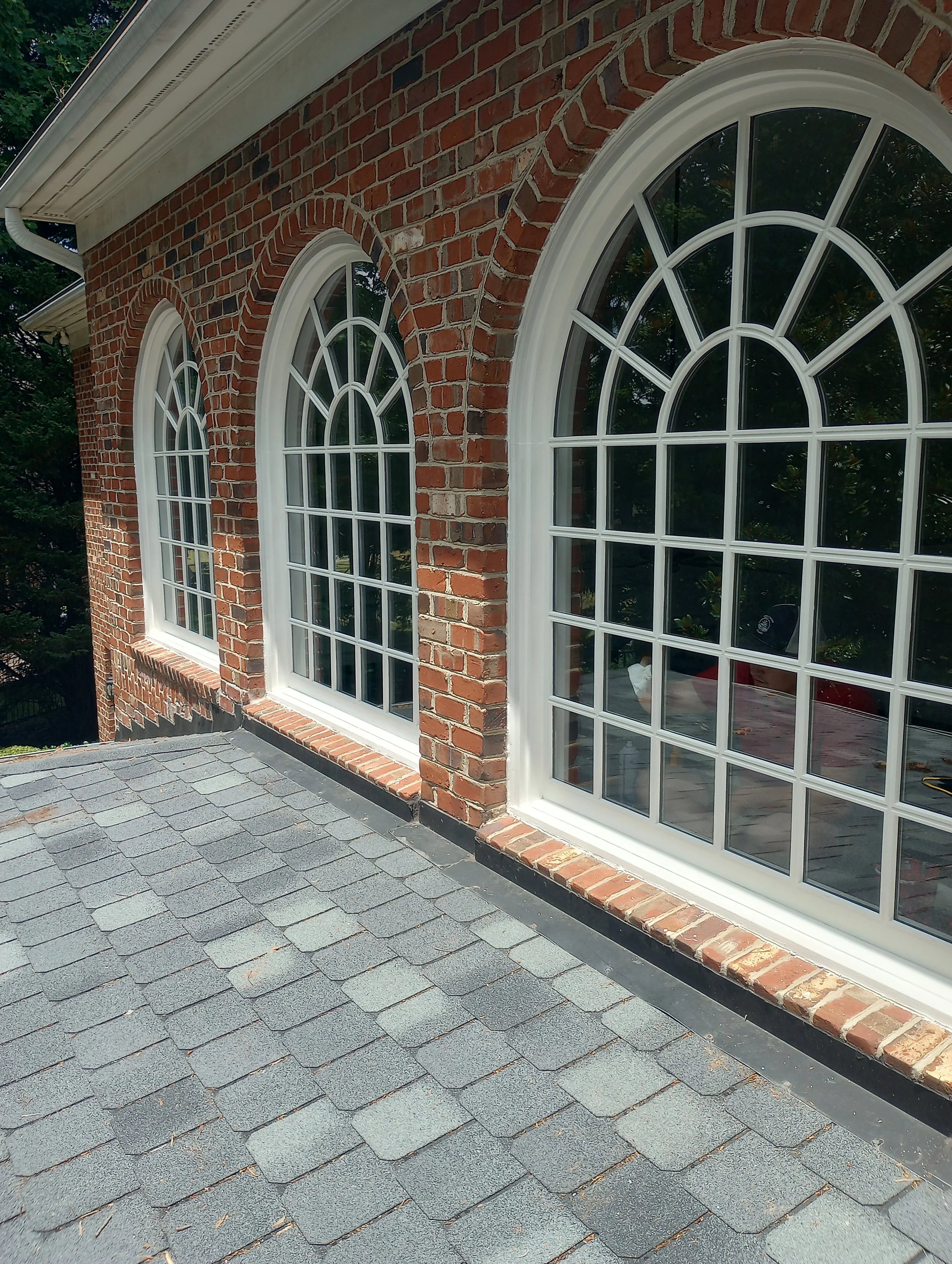 Close-up view of brick exterior wall with three large arched windows and shingled roof.