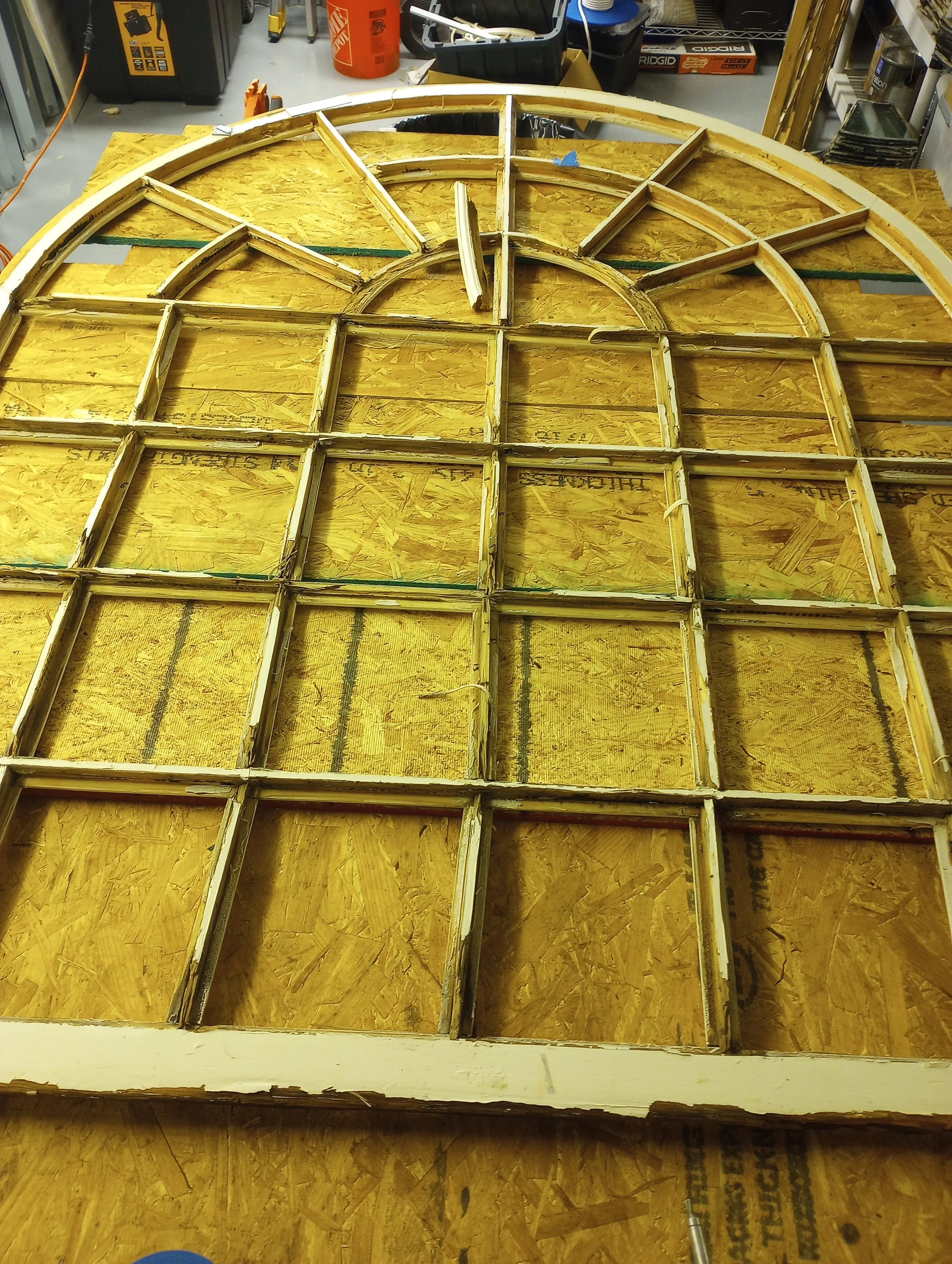 A wooden framework for a large clock face, with individual sections forming the clock's design, is laid out on a workbench in a workshop.