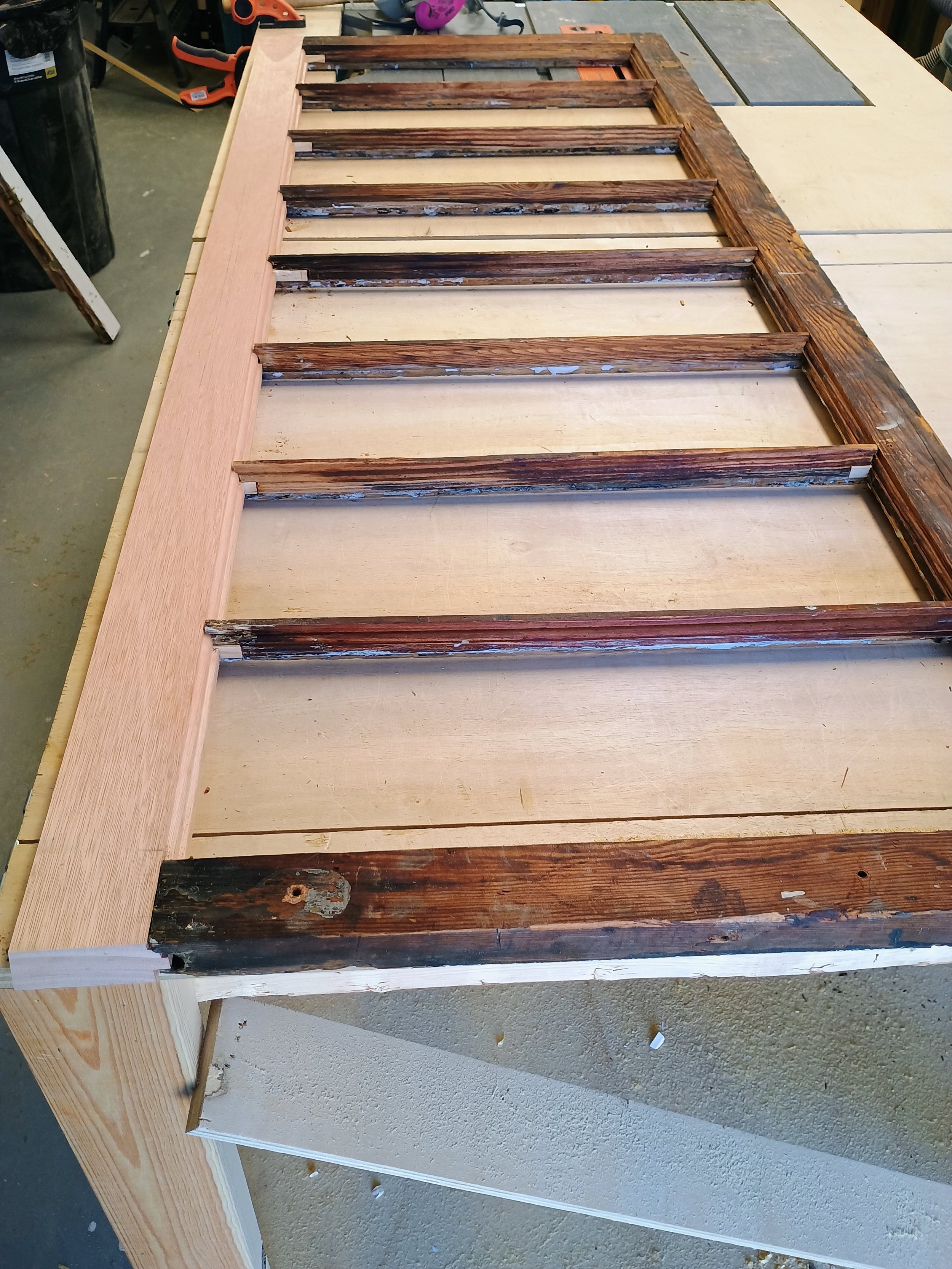 Wooden frame with vertical and horizontal slats, some of which are aged and weathered, lying on a workbench in a workshop.