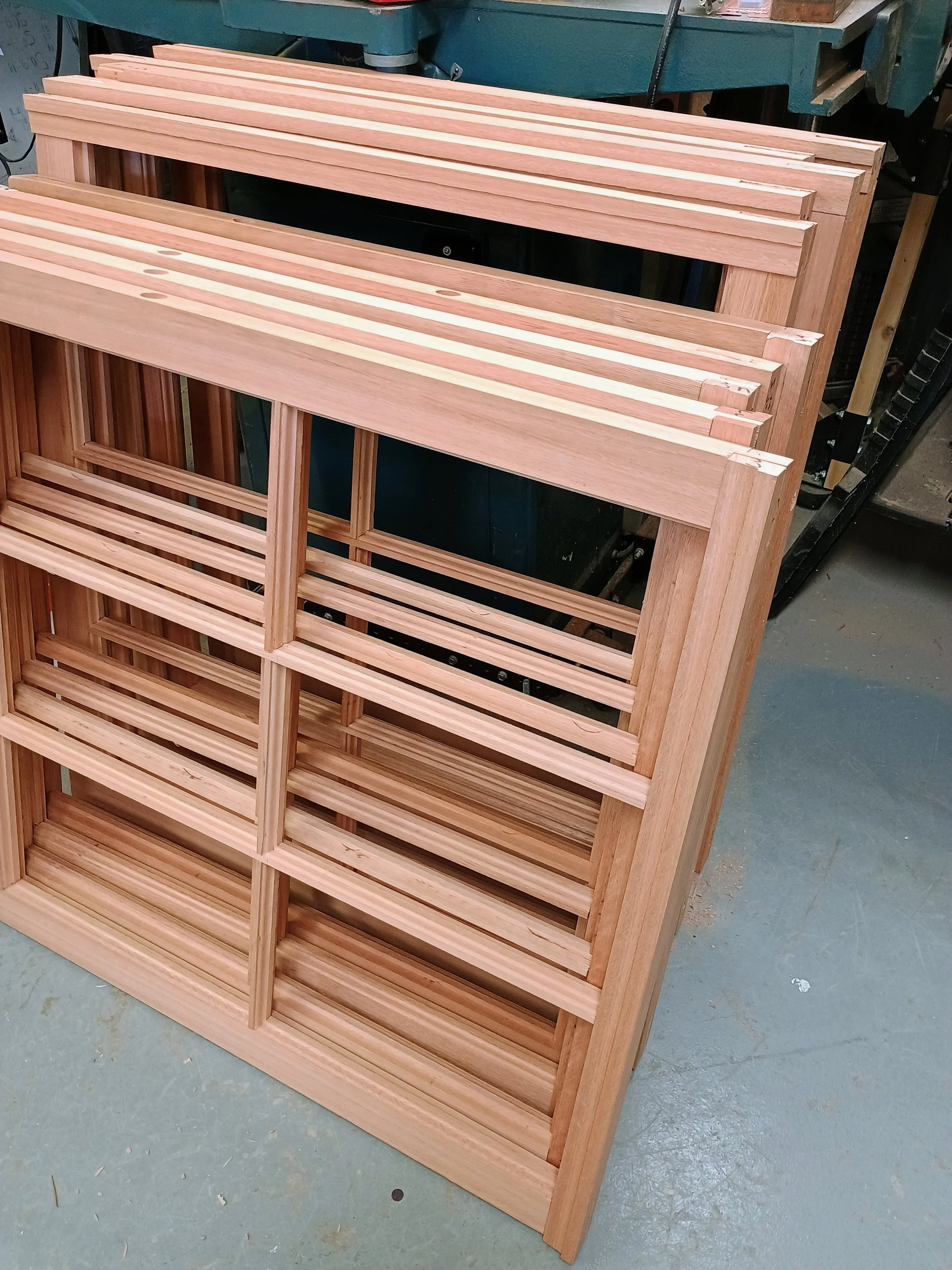 Wooden wine rack with multiple shelves made of light-colored wood, placed in a workshop.
