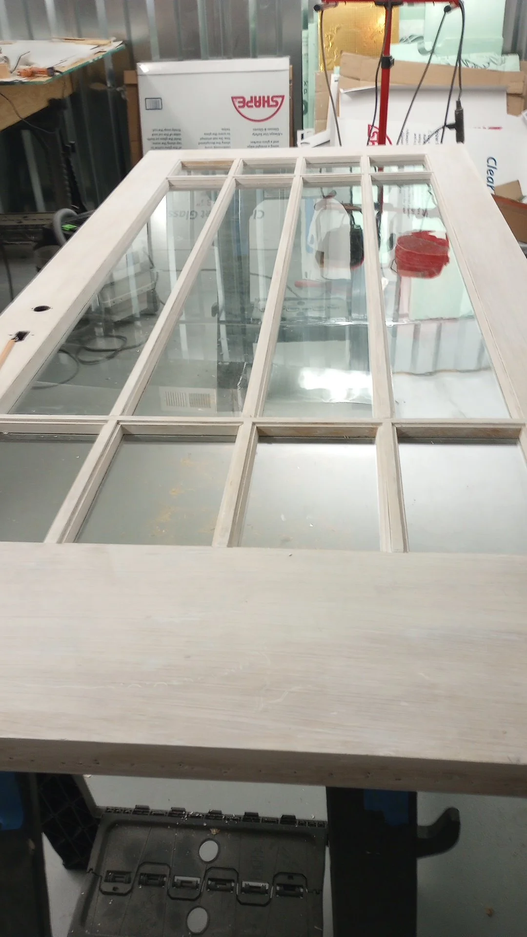 A wooden door with glass panes laying flat on a workbench in a workshop.