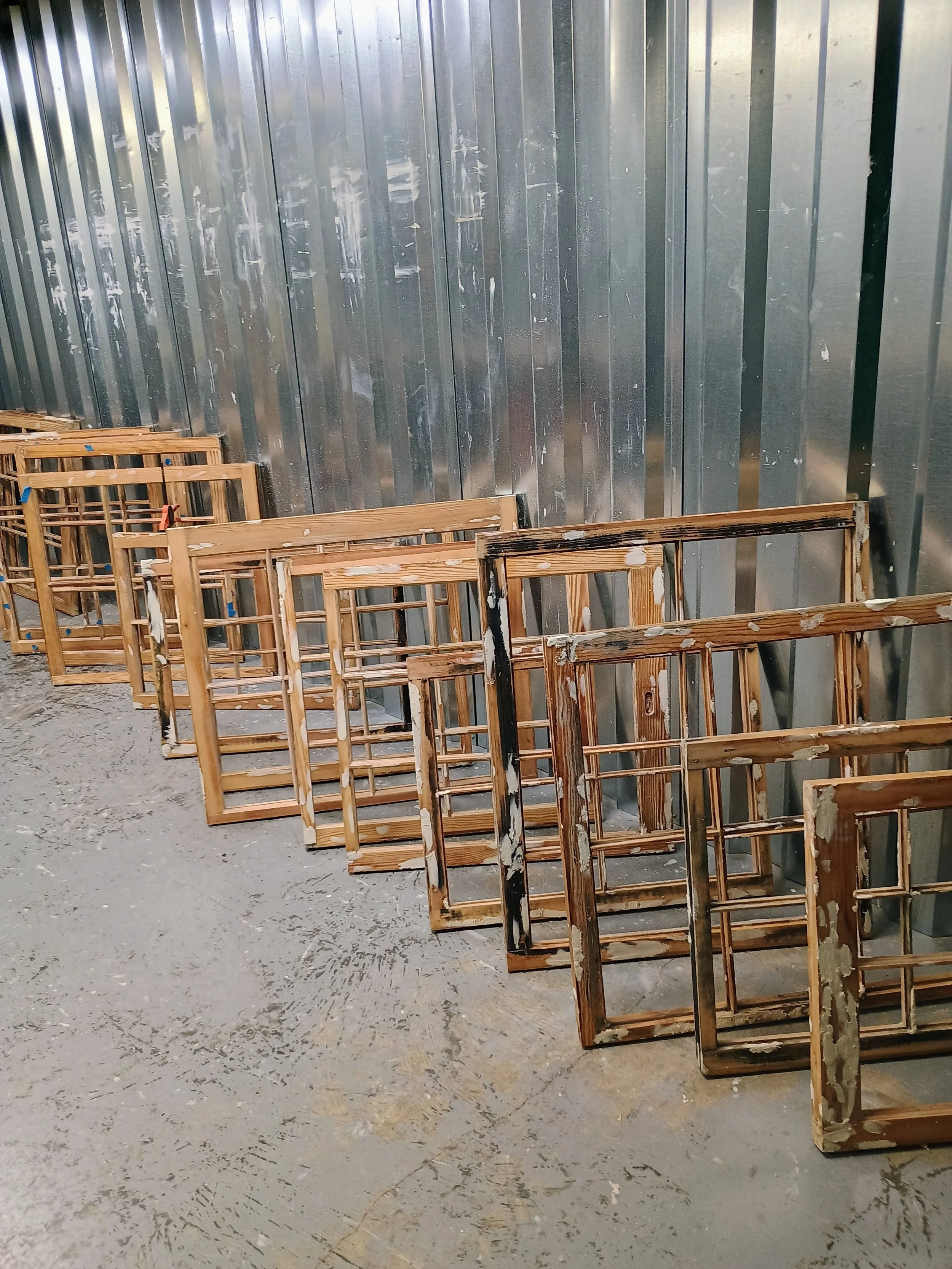 Multiple wooden chairs stacked against a metallic wall in a warehouse or storage area.