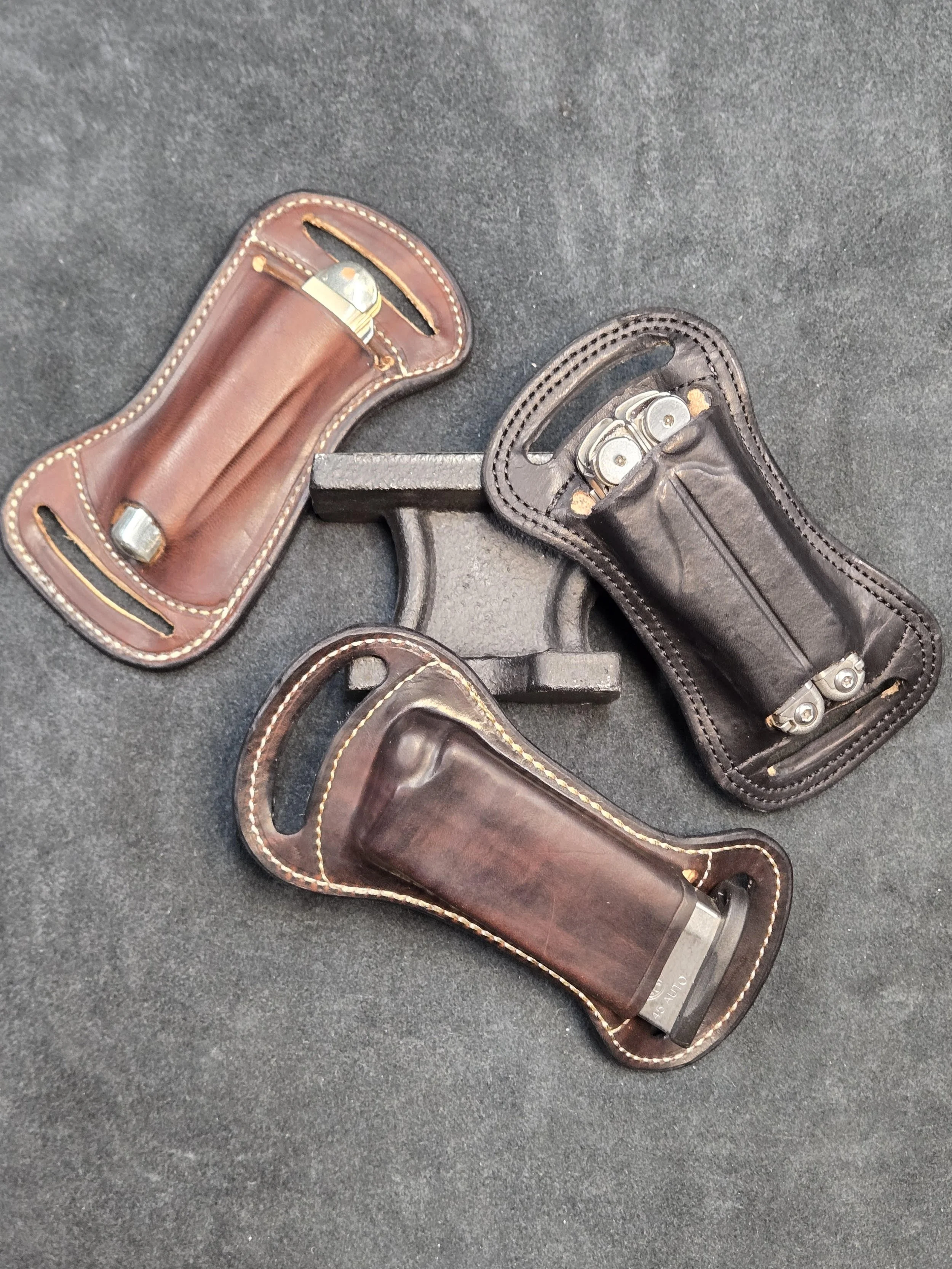 Three leather utility holsters placed on a dark surface with a metal stand.