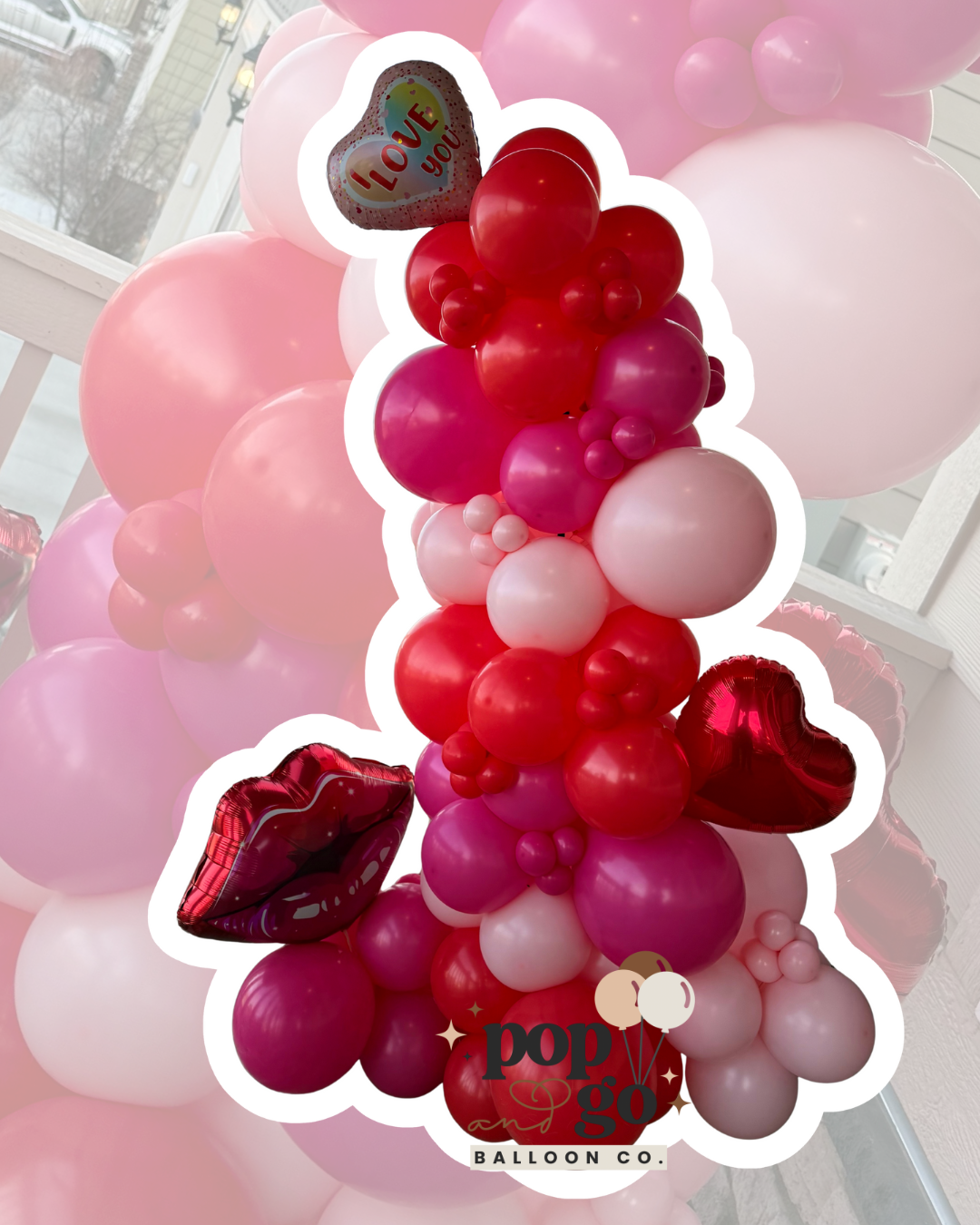 A large balloon arrangement consisting of pink, red, and white balloons with a heart-shaped "I Love You" balloon and red lips-shaped balloons, decorated for a romantic occasion.