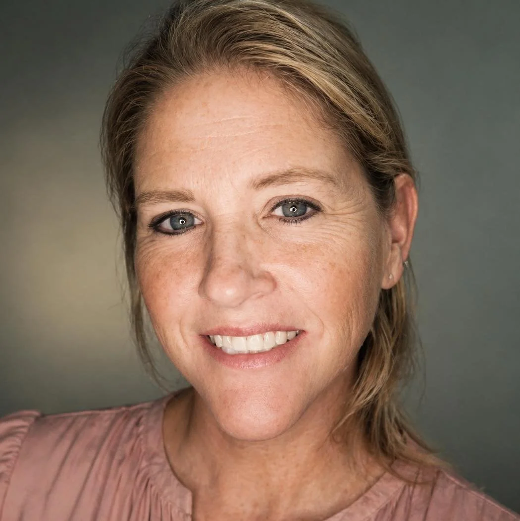 Close-up portrait of a smiling woman with blonde hair, blue eyes, and light skin, wearing a pink top.