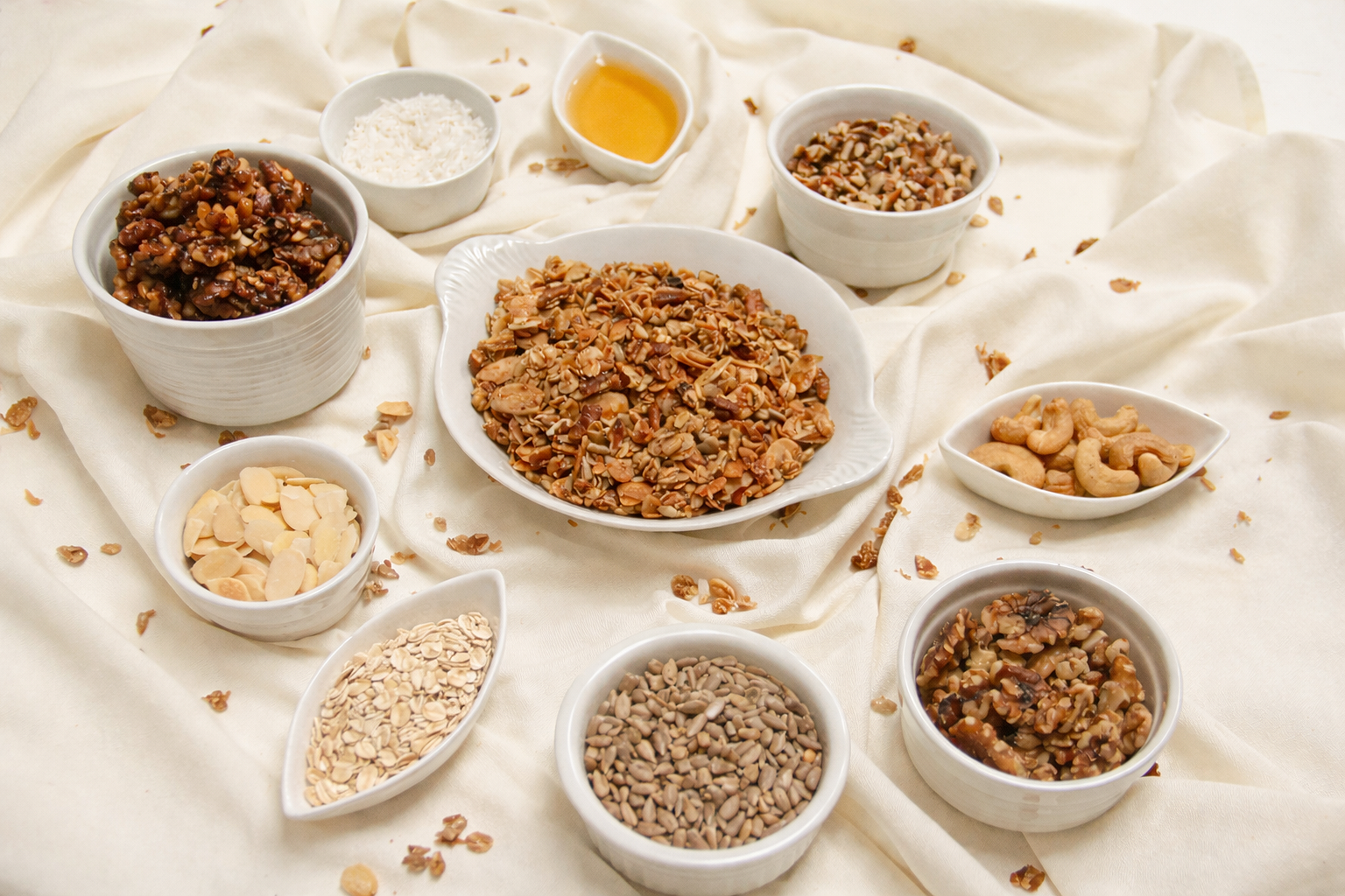 Various bowls of mixed nuts and dried fruit on a cream-colored cloth.