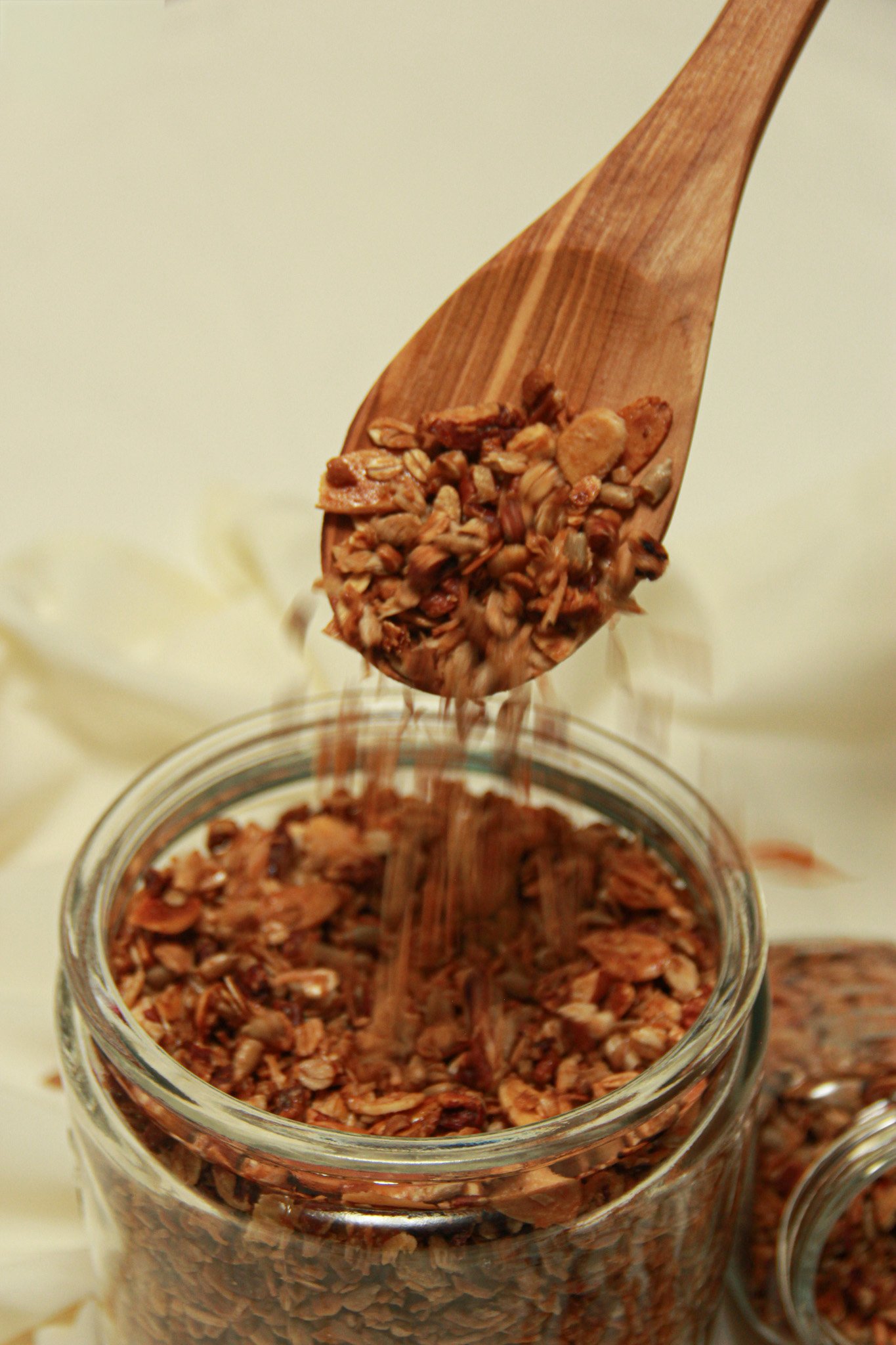 Close-up of granola being scooped from a glass jar with a wooden spoon.