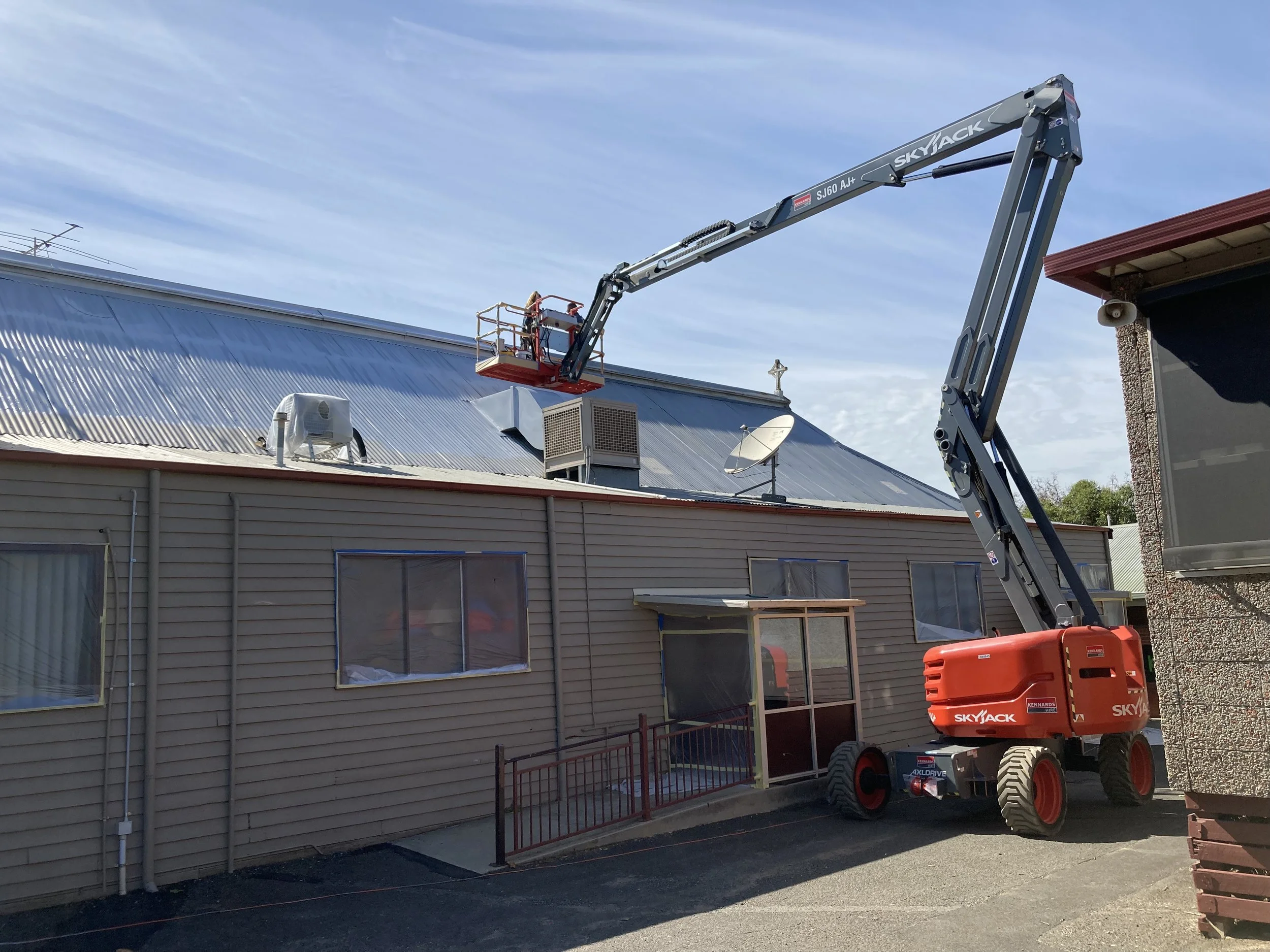 Roof painting services using a red skyjack boom lift