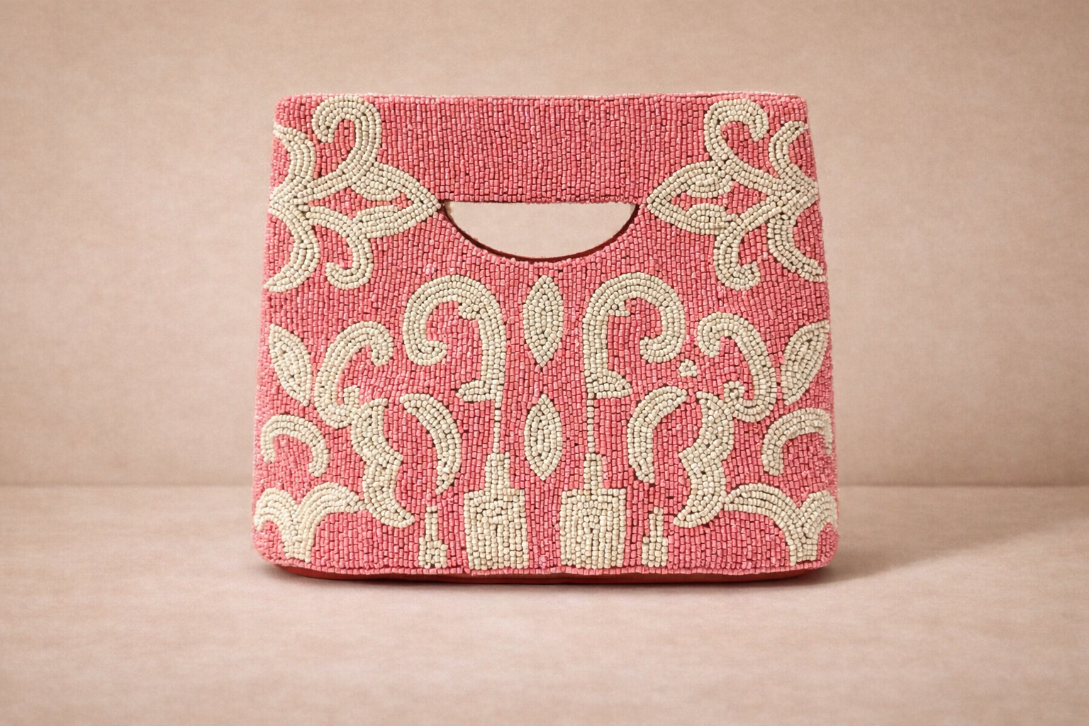 Pink beaded handbag with intricate white floral and scroll patterns on a beige background.
