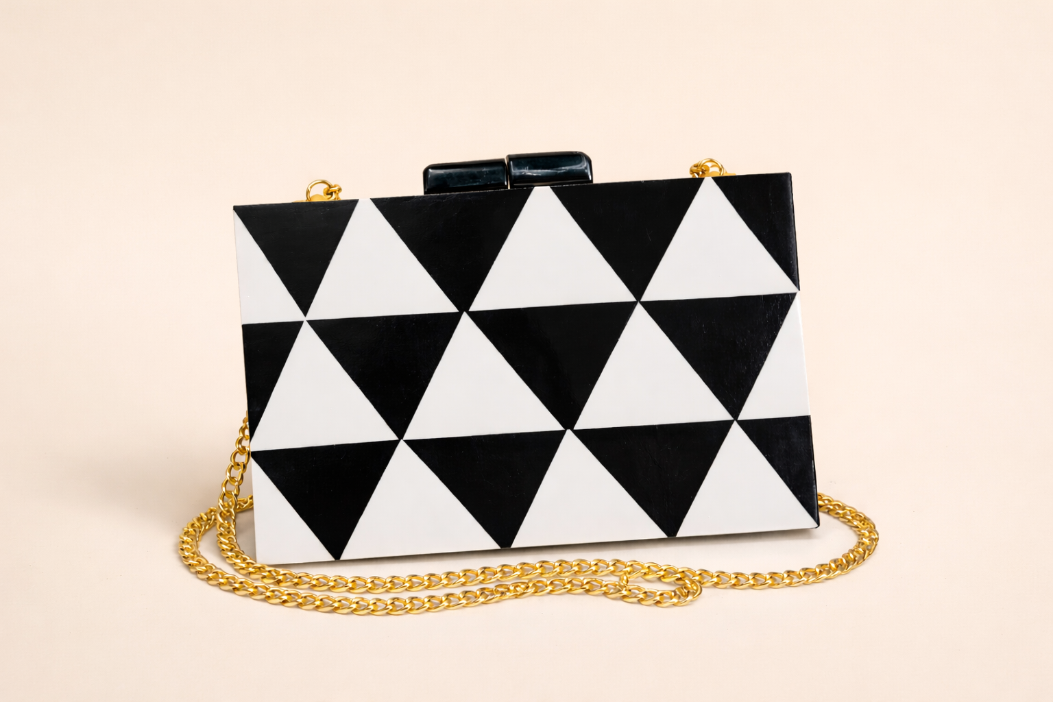 A black and white geometric patterned clutch purse with a gold chain strap on a beige background.