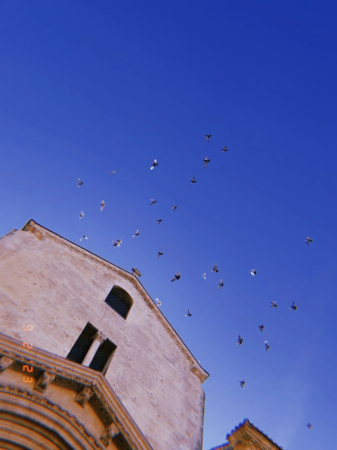 Birds flying in a clear blue sky above a historic stone building.