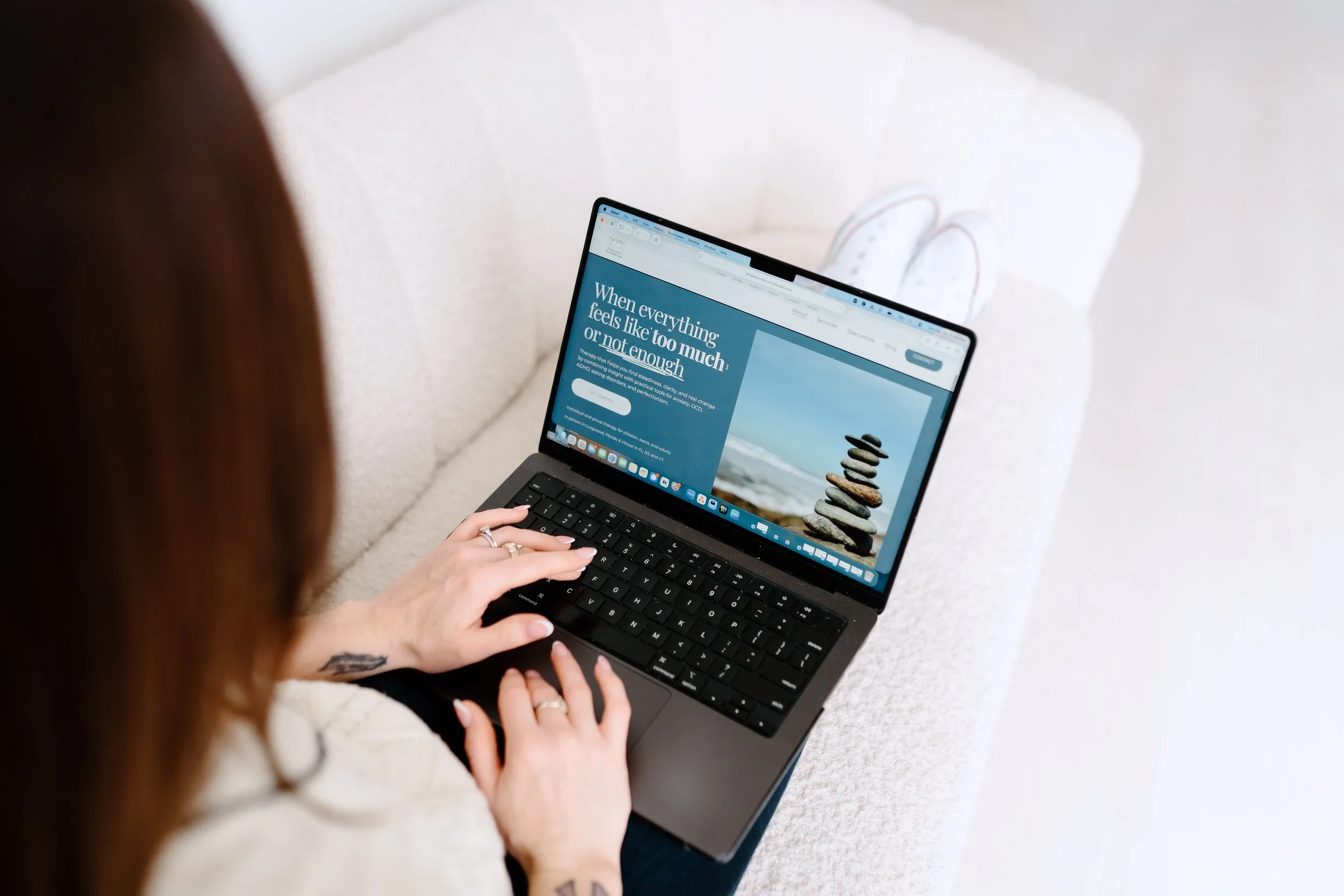 Person using a laptop on a white sofa, with a webpage about mental health visible on the screen.