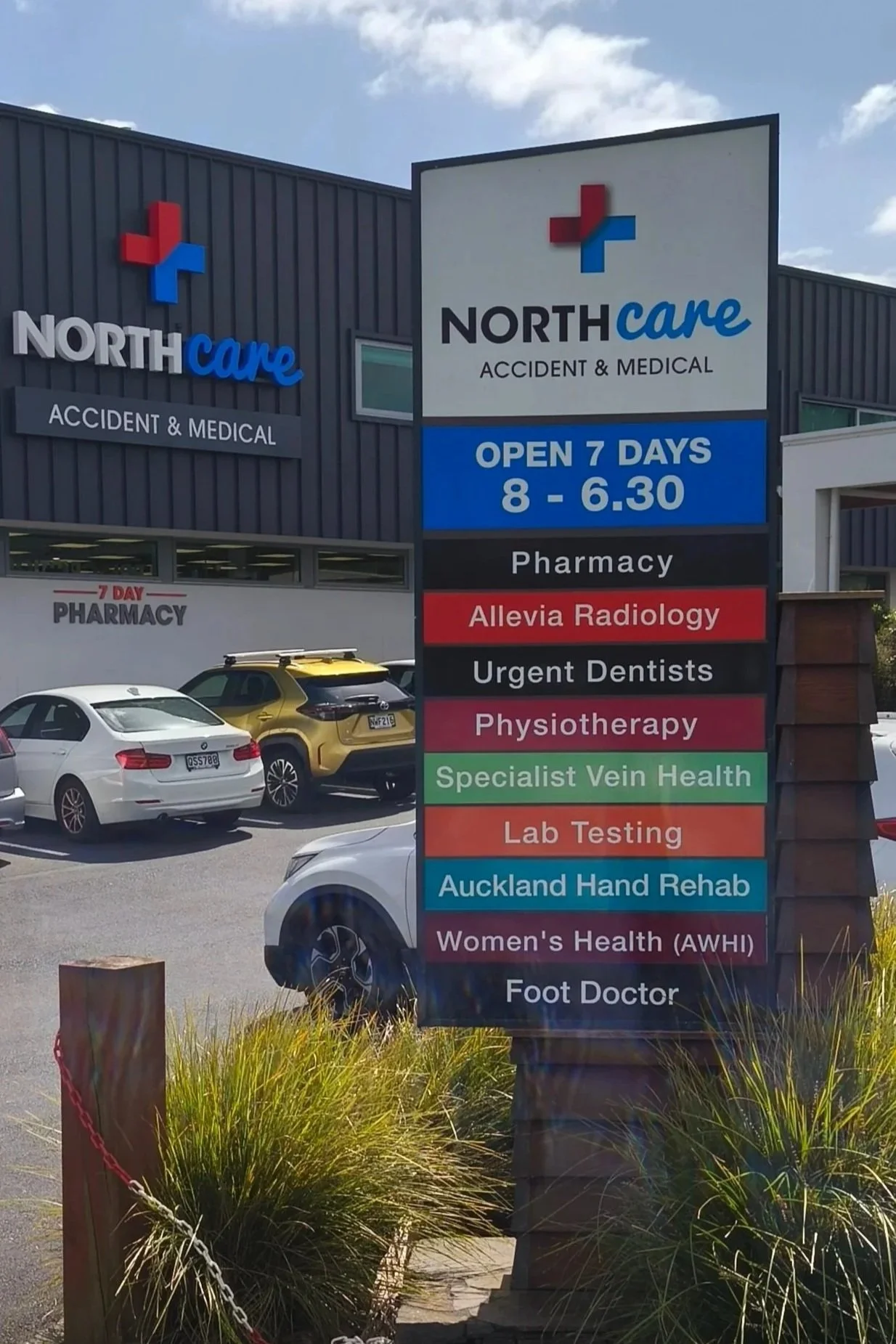 Signboard outside Northcare Accident & Medical clinic showing services such as pharmacy, Allevia radiology, urgent dentists, physiotherapy, specialist vein health, lab testing, Auckland hand rehab, women's health, and foot doctor, with business hours open 7 days from 8 AM to 6:30 PM.