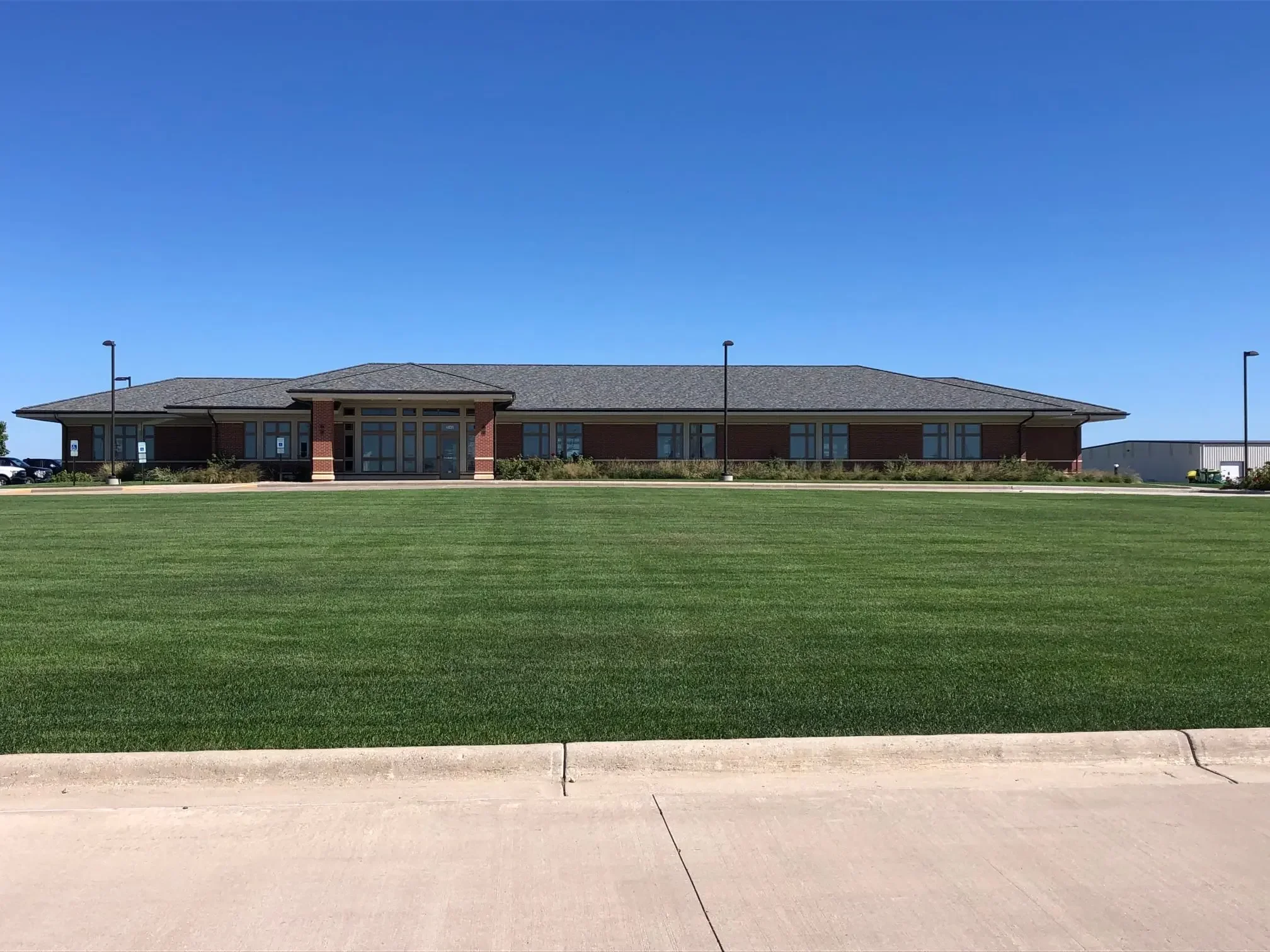 Single-story brick building with large windows and a main entrance, surrounded by a grassy lawn, under a clear blue sky.