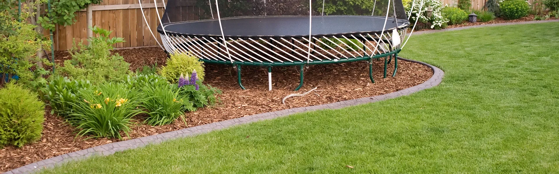 Custom concrete edging framing trampoline in backyard