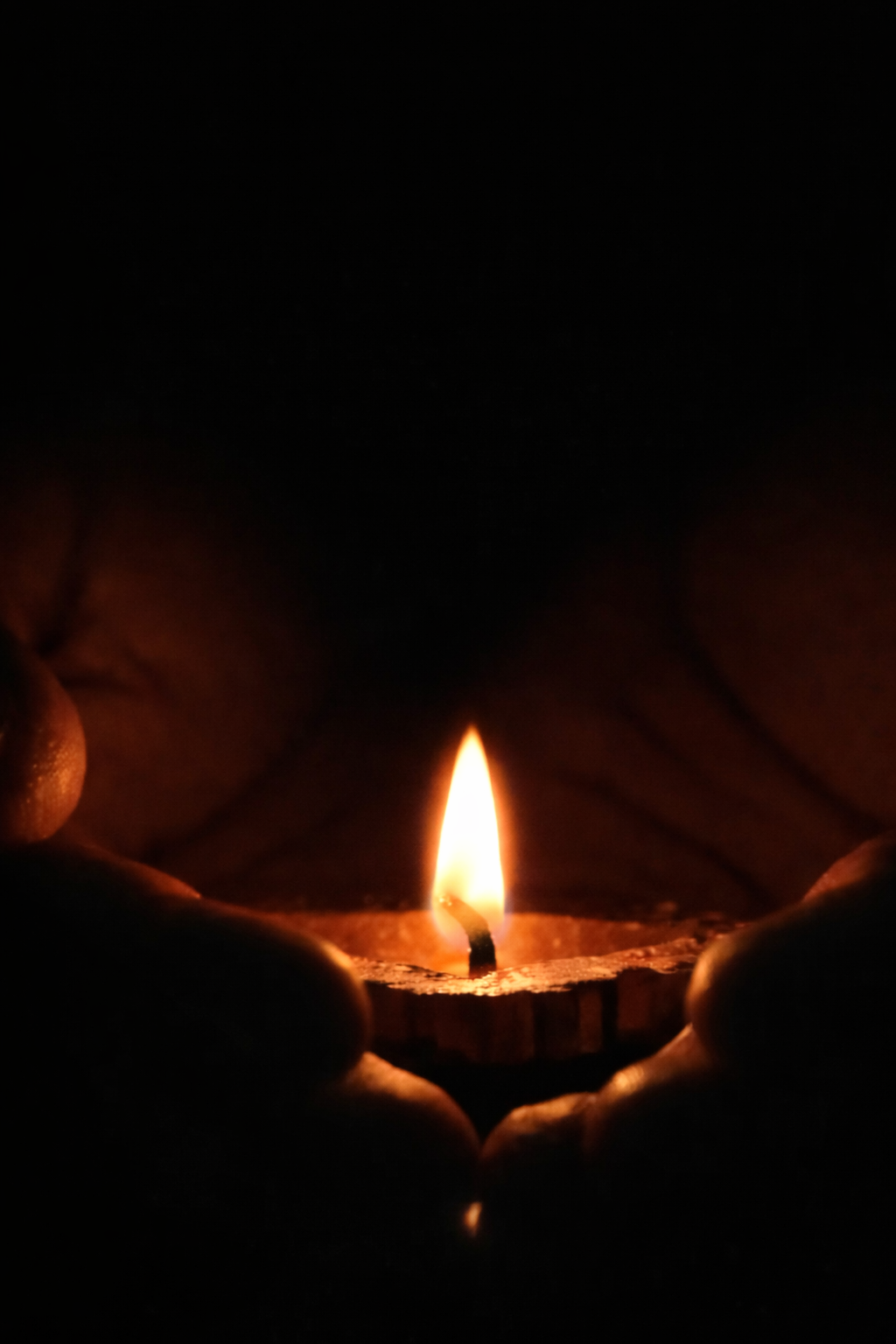 Manos sosteniendo una vela encendida en la oscuridad.