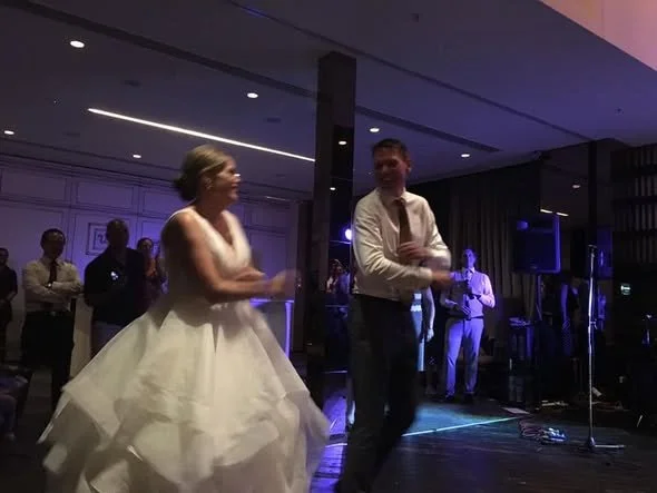 A bride and groom dancing at their wedding reception with wedding guests in the background.