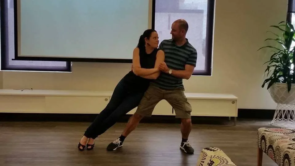 A man and woman are dancing together learning their wedding dance, at a space in their office.