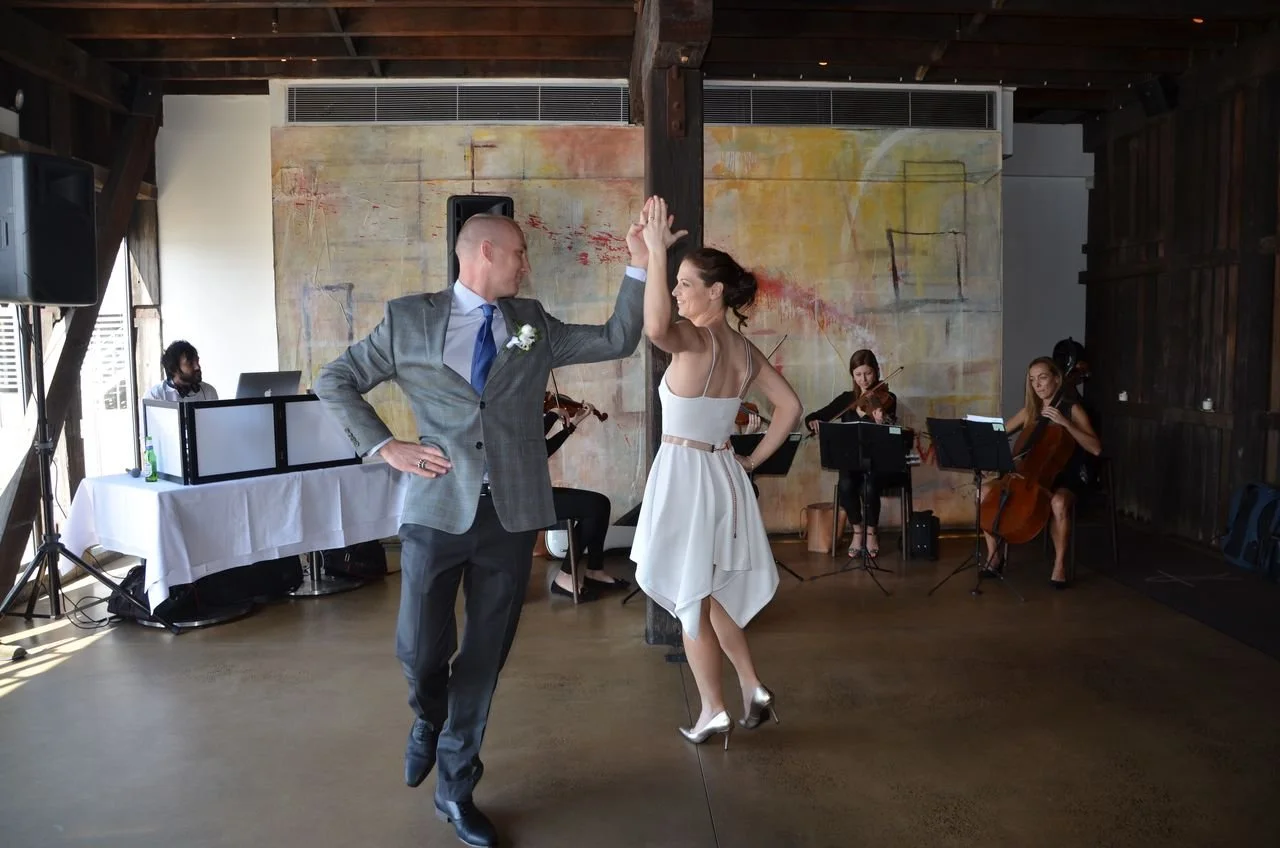 A bride and groom dancing the tango together at their wedding reception, with a string quartet playing music in the background.