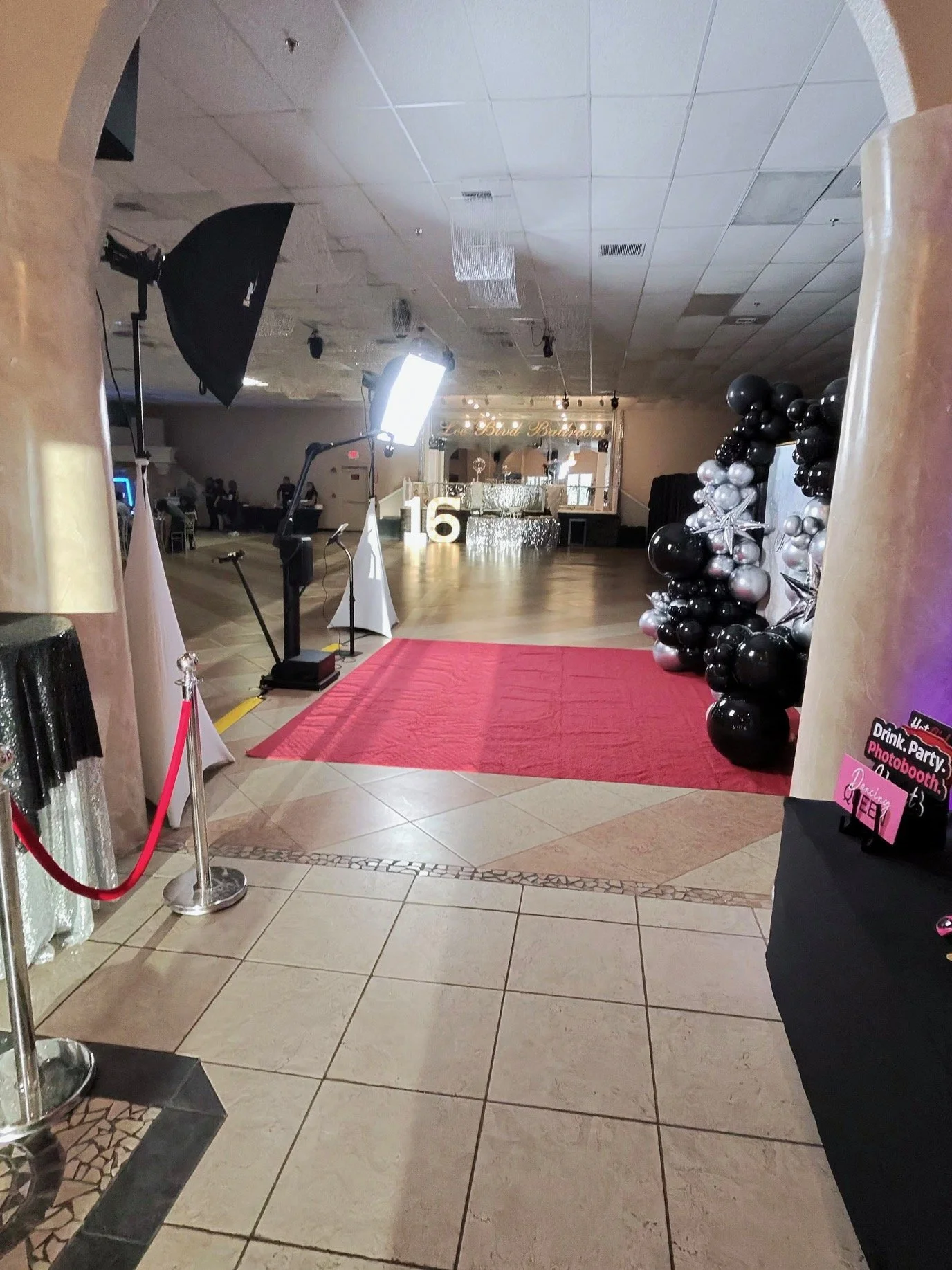 Event venue decorated with balloons, a red carpet, and photo booth signs, set up for a party or celebration. Photography lighting equipment is visible, Glambot ready to go.